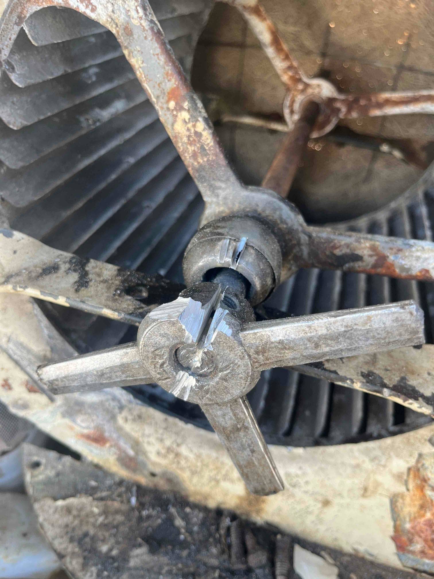 Close-up of a blower wheel assembly with a cracked metal hub and rusted supports inside the housing.