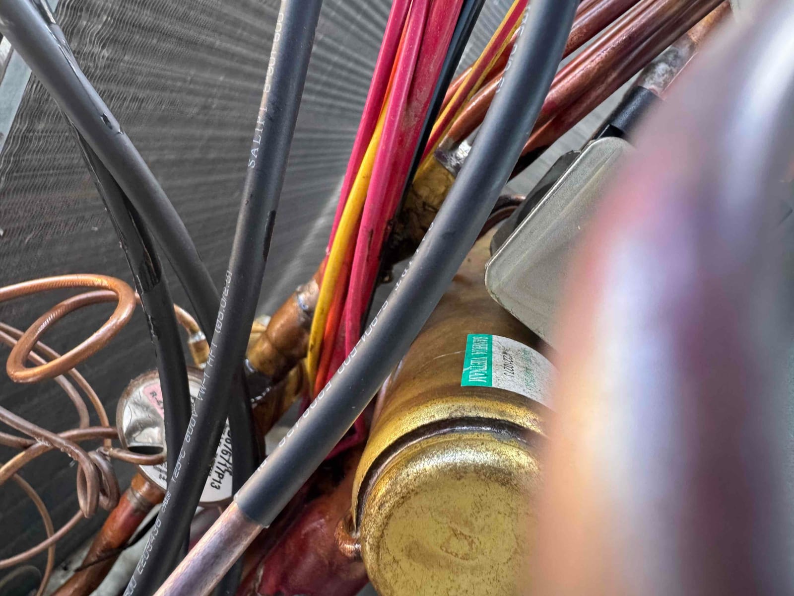 Close-up of compressor body with wiring bundles and copper refrigerant lines inside the condenser cabinet.