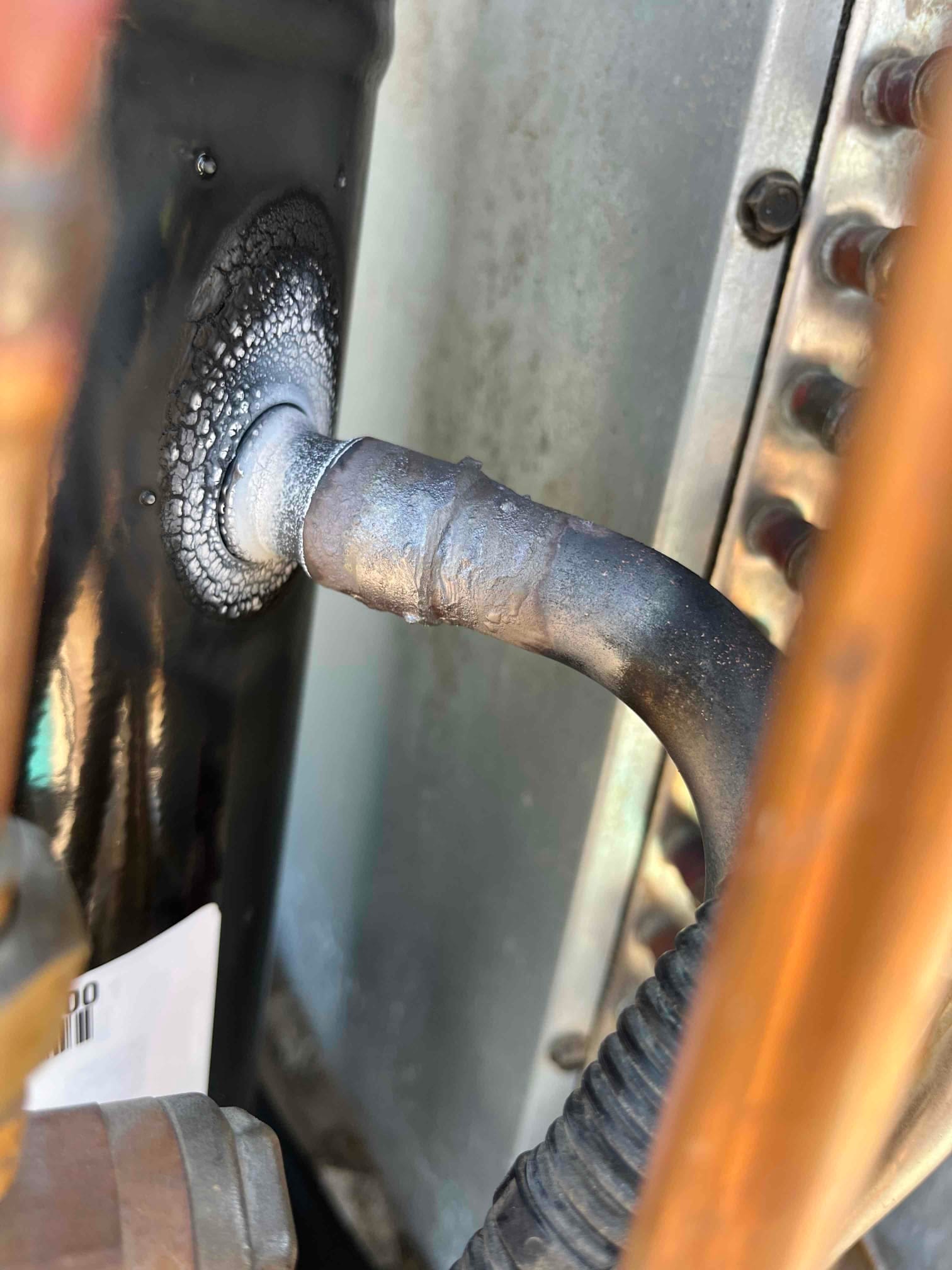 Close-up of a compressor refrigerant line connection showing frost and residue at the brazed joint inside the unit.