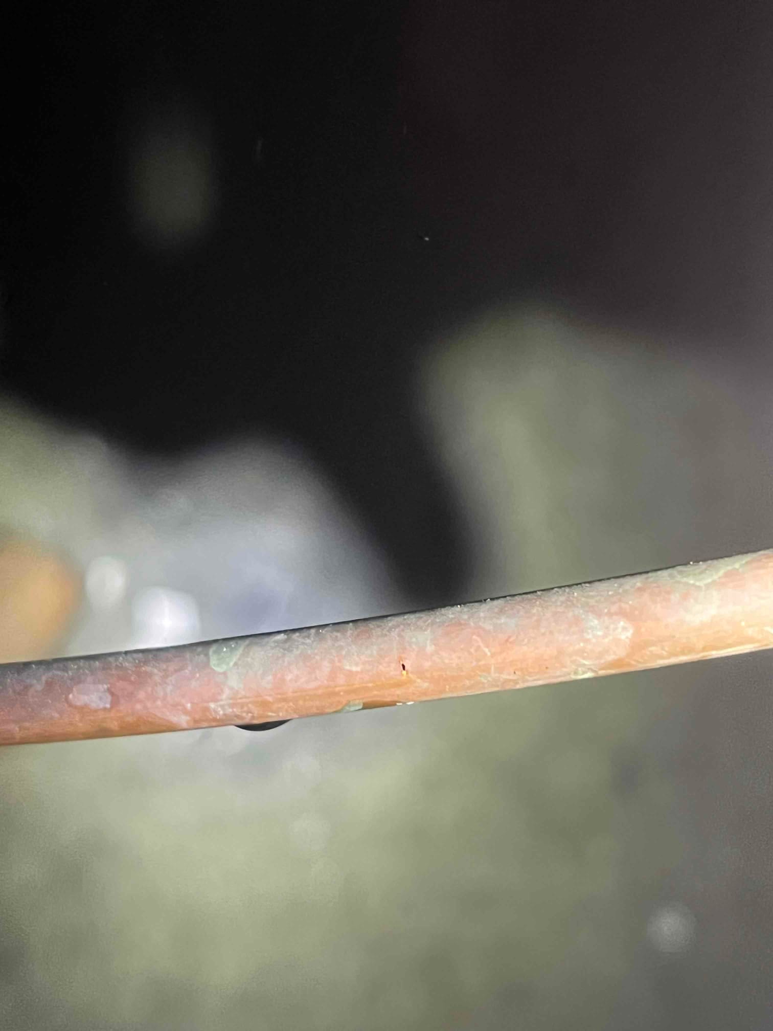 Close-up of copper tubing showing a small pinhole and a bead of moisture along the surface.