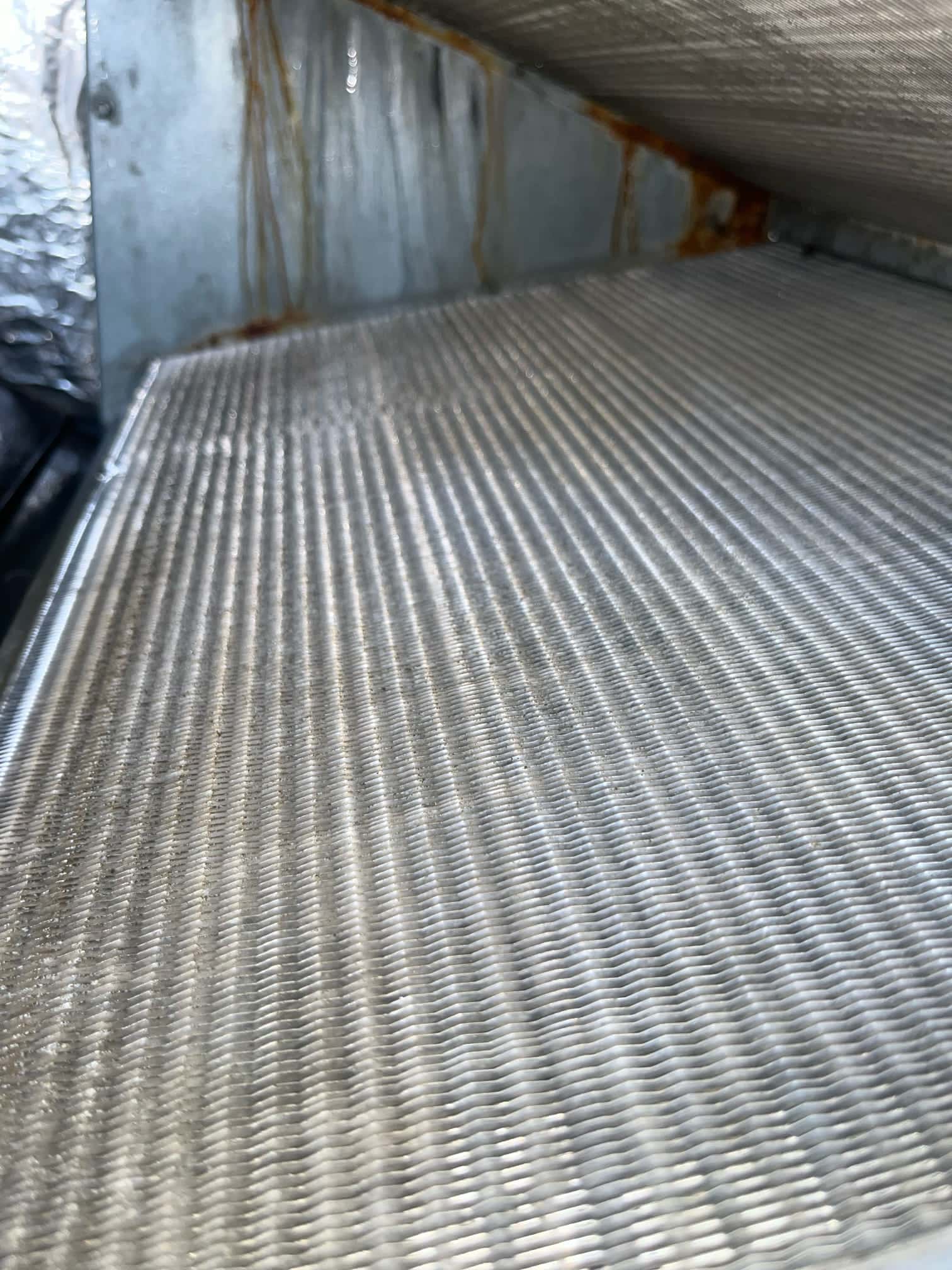 Close-up of an evaporator A-coil inside the air handler, showing clean aluminum fins and rust-stained cabinet surfaces.