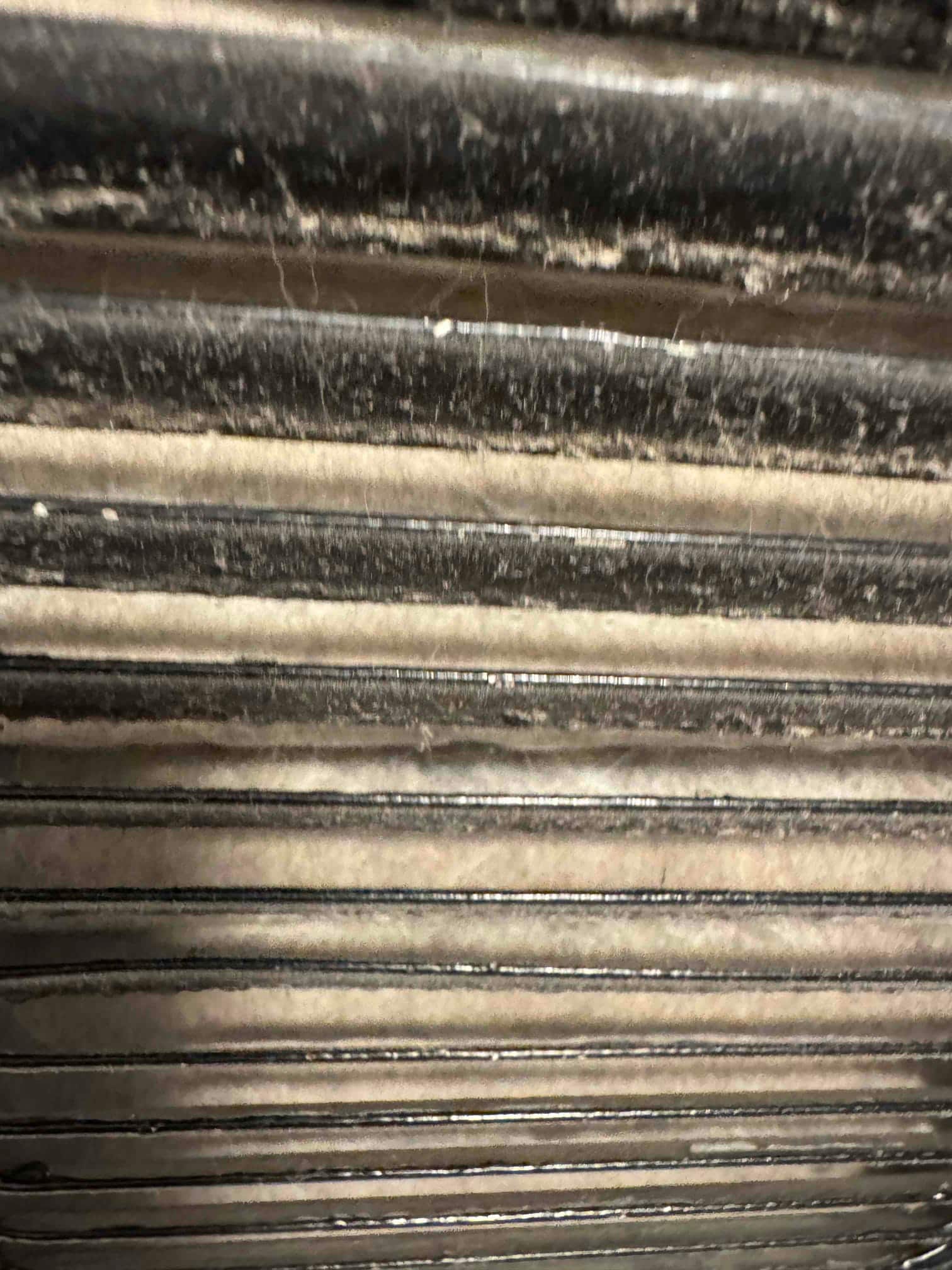 Close-up of HVAC coil fins showing visible dust and lint accumulation along the horizontal channels.