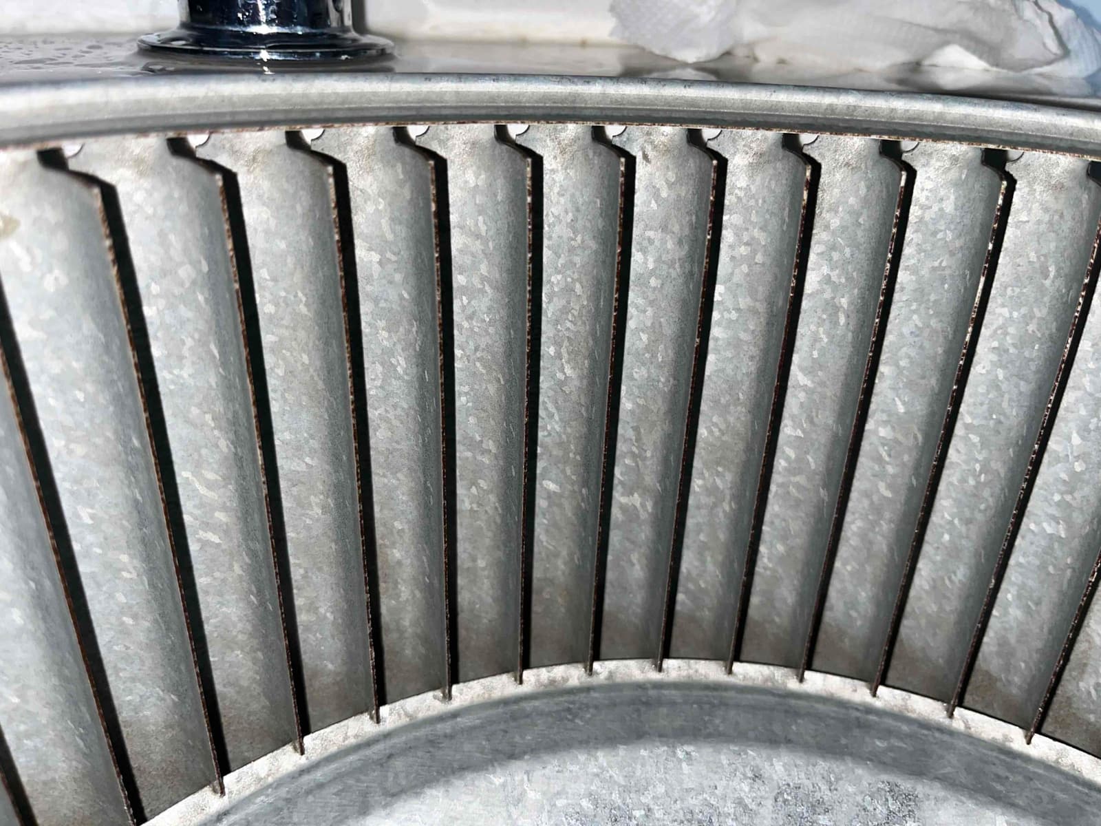 Close-up of a metal blower wheel showing clean, galvanized fins and the circular housing edge.