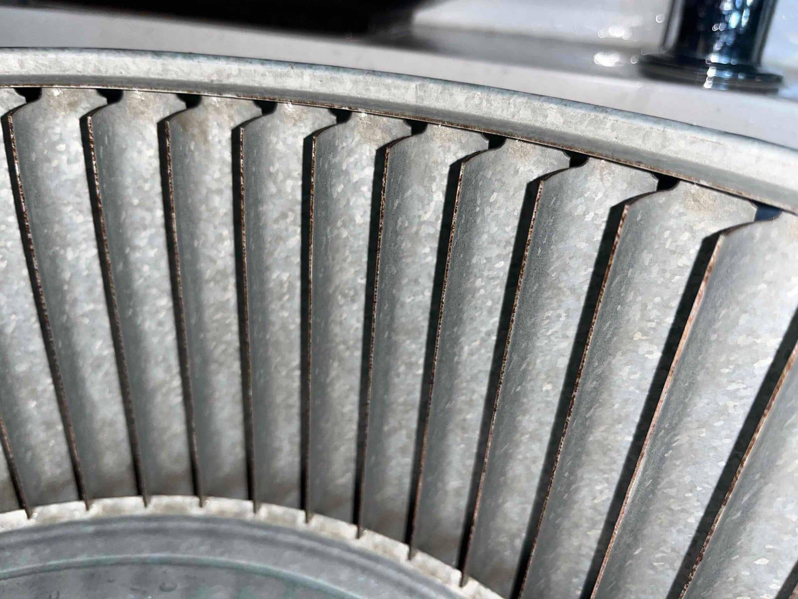Close-up of a metal blower wheel with evenly spaced fins and hub visible at the bottom.