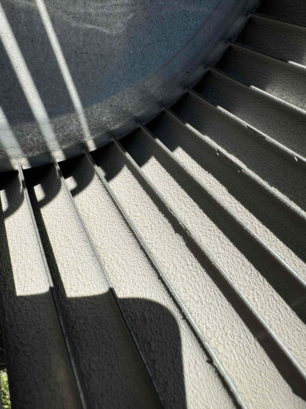 Close-up of a metal blower wheel showing multiple straight vanes and a circular hub under direct sunlight.