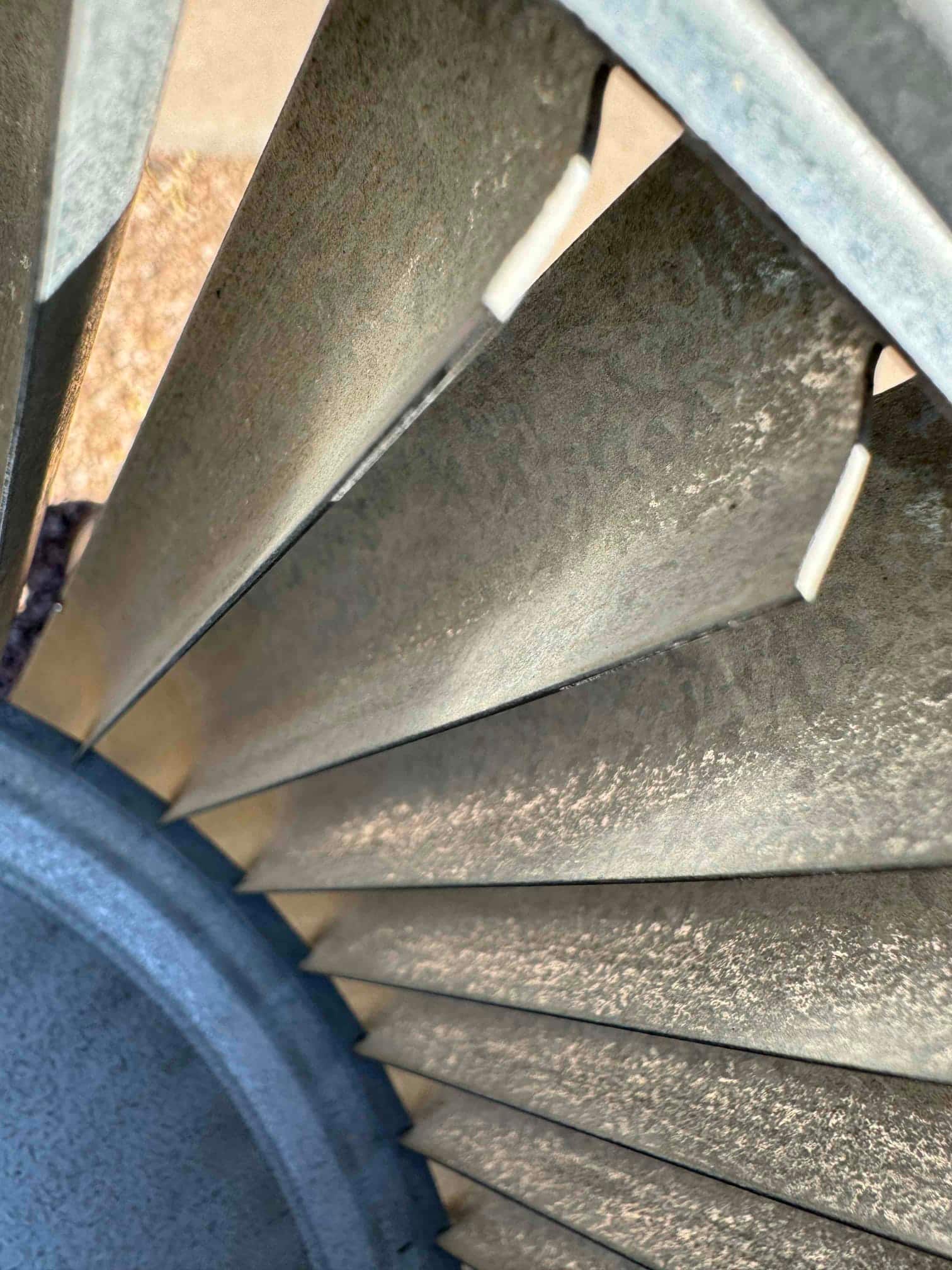 Close-up of a metal centrifugal blower wheel showing multiple evenly spaced fins inside the housing.