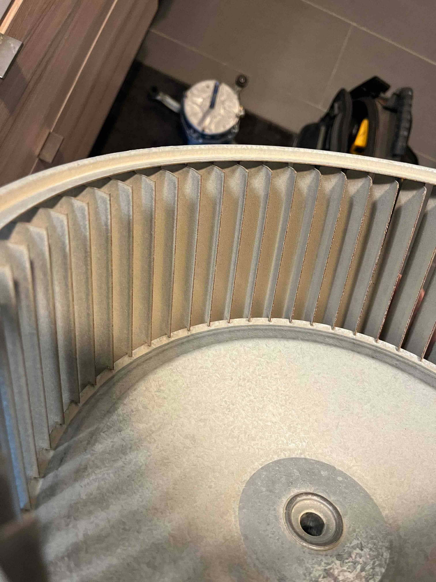 Close-up of a metal HVAC blower wheel, showing the fins and central hub inside the squirrel-cage assembly.