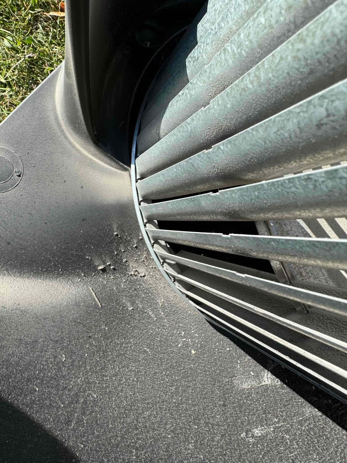 Close-up of an outdoor condenser fan guard and shroud with surface dust and small debris near the opening.