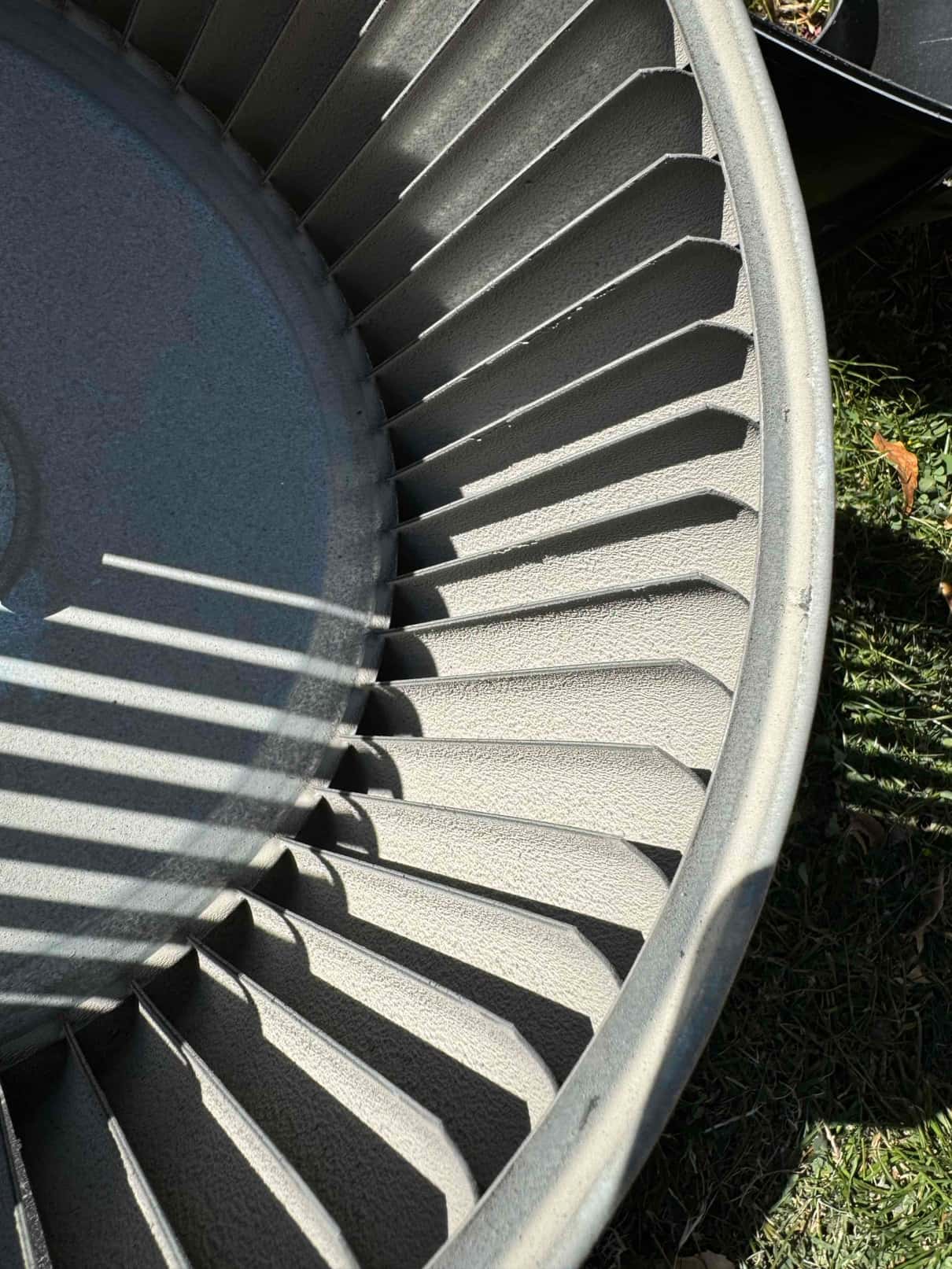 Close-up of a residential HVAC blower wheel outside the unit, showing multiple forward-curved blades and rim.