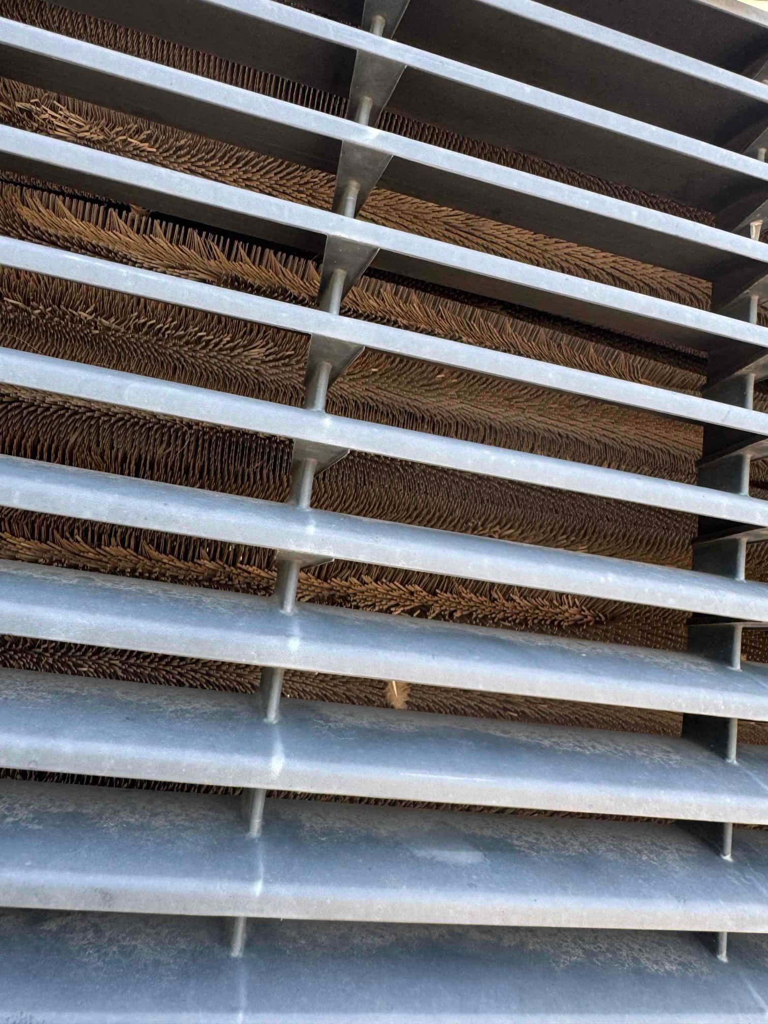 Close-up view through a louvered metal grille showing condenser coil fins behind the protective cover.