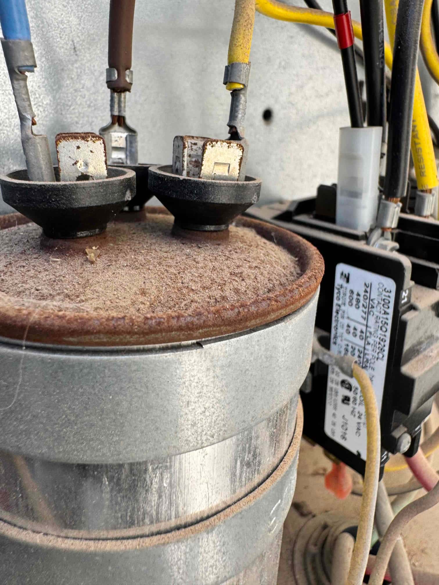 Compressor electrical terminals with brown, blue, and yellow wires; rubber terminal boots; rust and dust on housing.