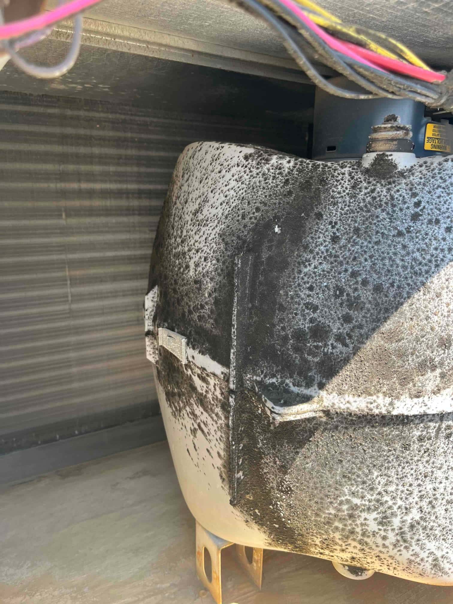 Compressor housing inside the condenser cabinet shows extensive black corrosion and surface staining, with wiring and coil visible nearby.