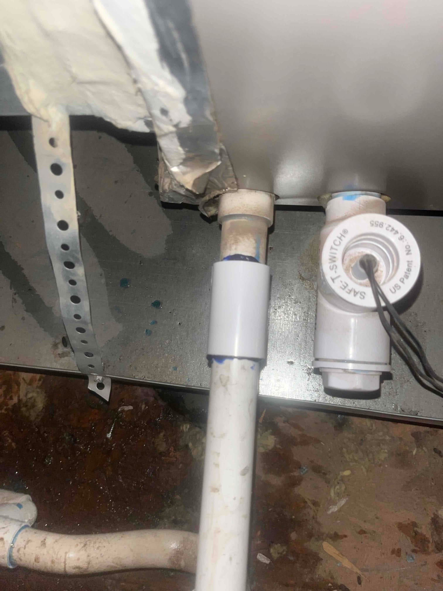 Condensate drain connections beneath the air handler, showing PVC piping, purple primer on fittings, and an inline float safety switch.