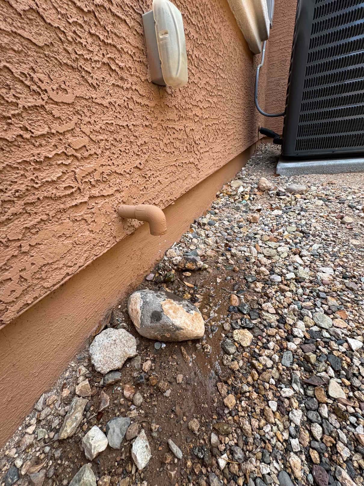 Condensate drain line discharges water onto the ground beside the outdoor condenser unit.