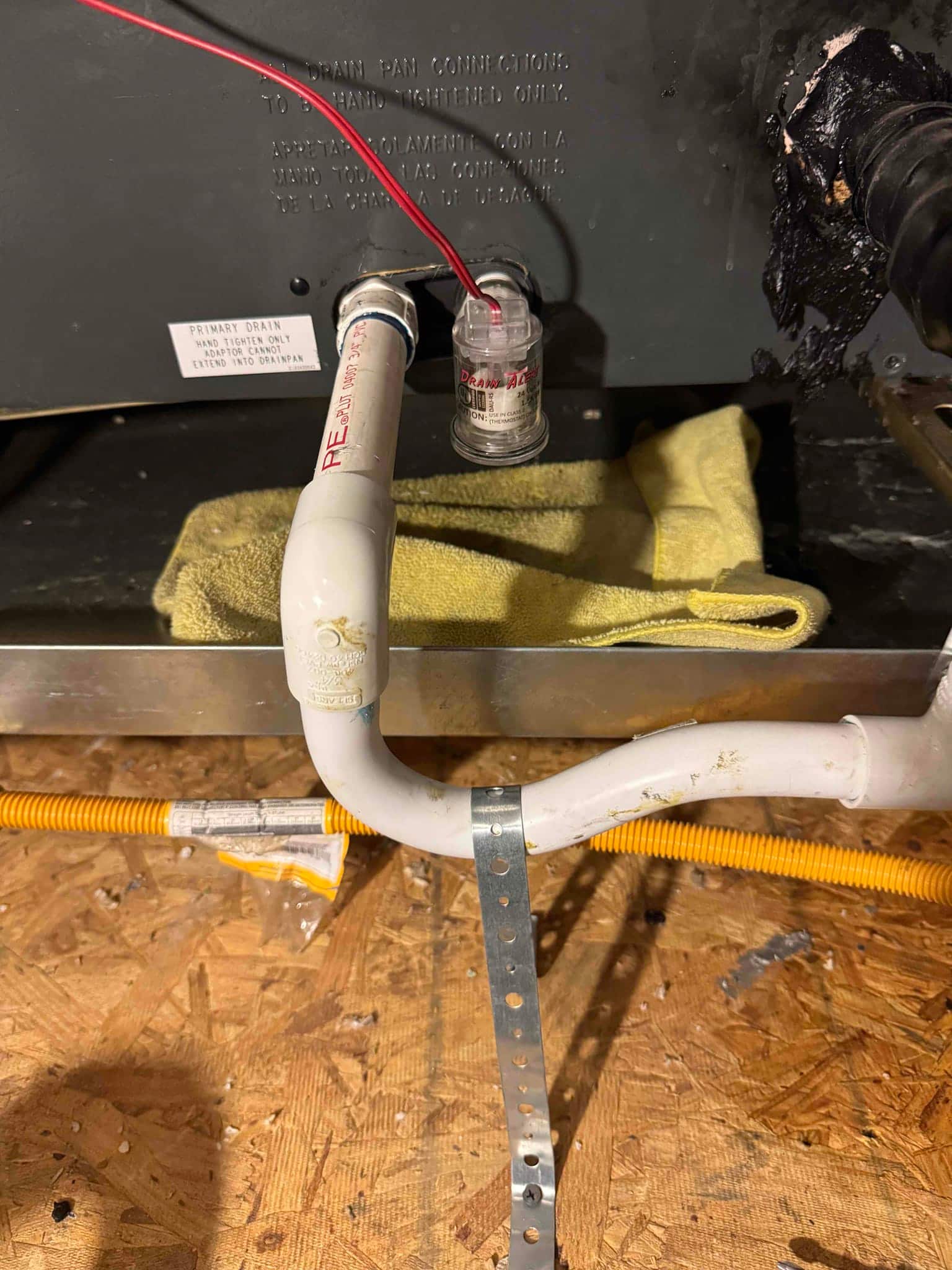 Condensate drain piping with inline float switch at air handler primary drain connection, secured with a metal strap.