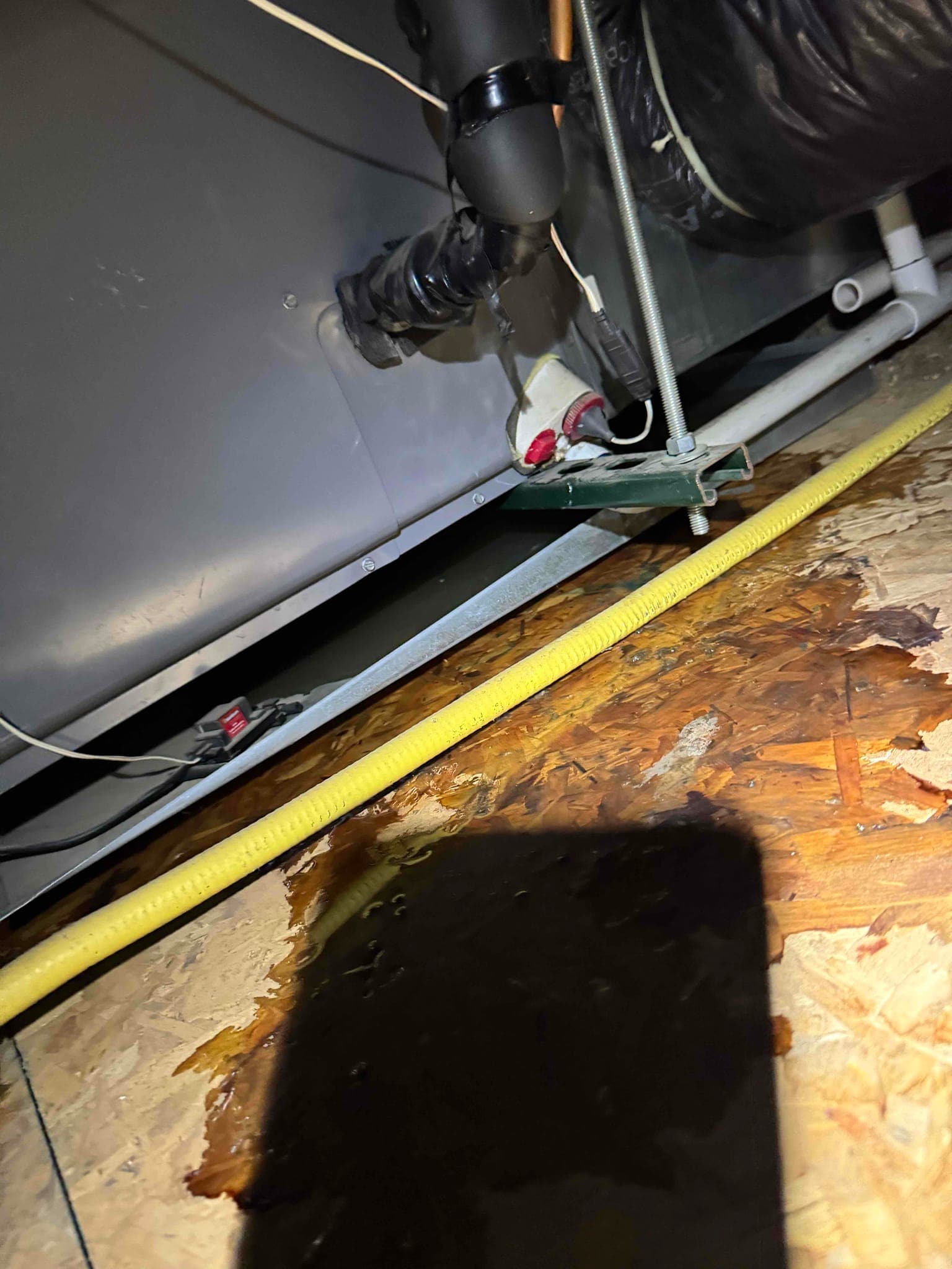 Condensate drain piping and trap beneath the air handler, with standing water on the attic floor.