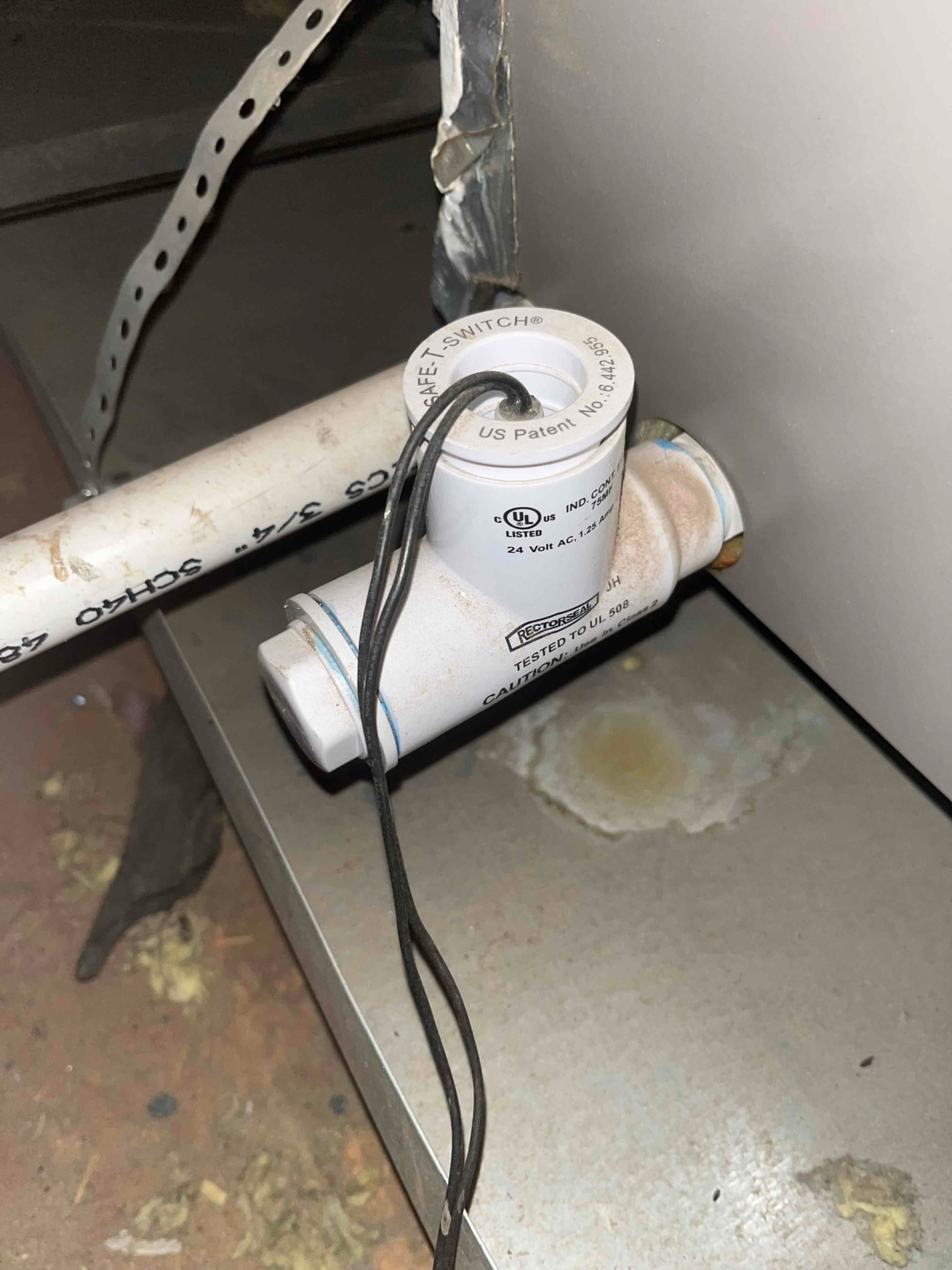 Condensate safety float switch on PVC drain tee with two low-voltage leads near the air handler.