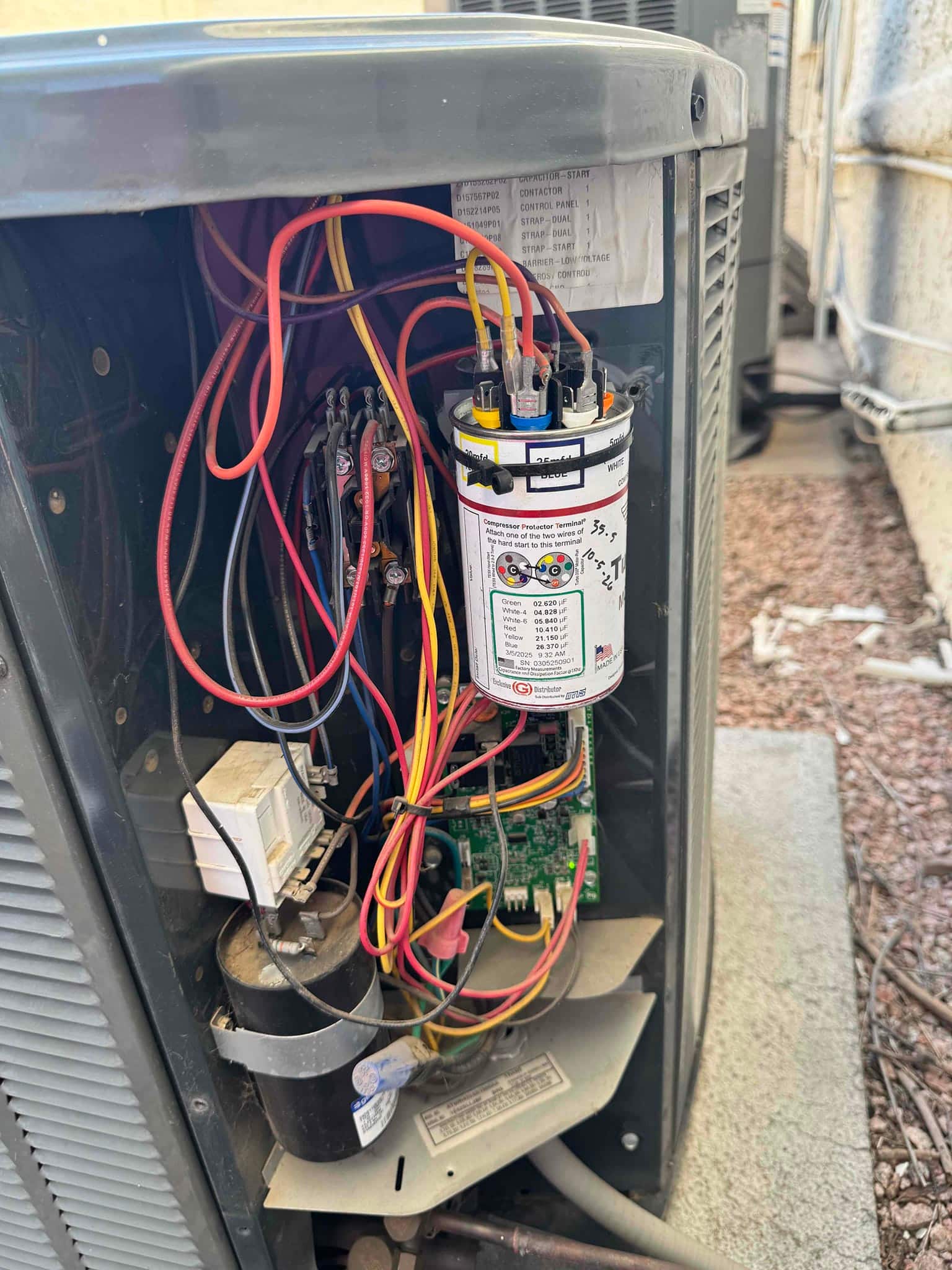 Condenser electrical compartment showing a dual-run capacitor, contactor, control board, and connected wiring with panel open.