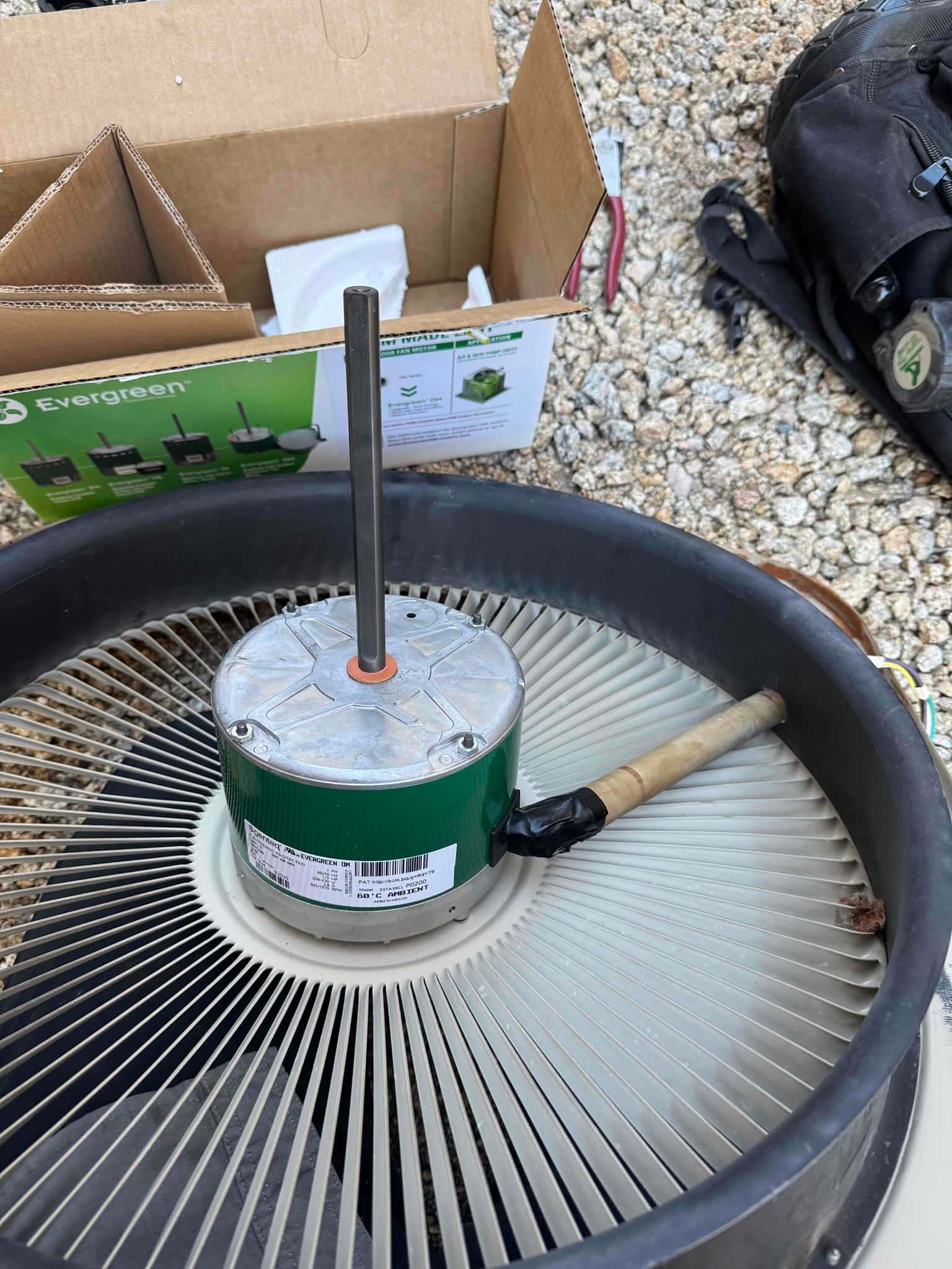 Condenser fan motor resting on the outdoor condenser fan blade assembly, with the shaft upright and wiring protected with tape.