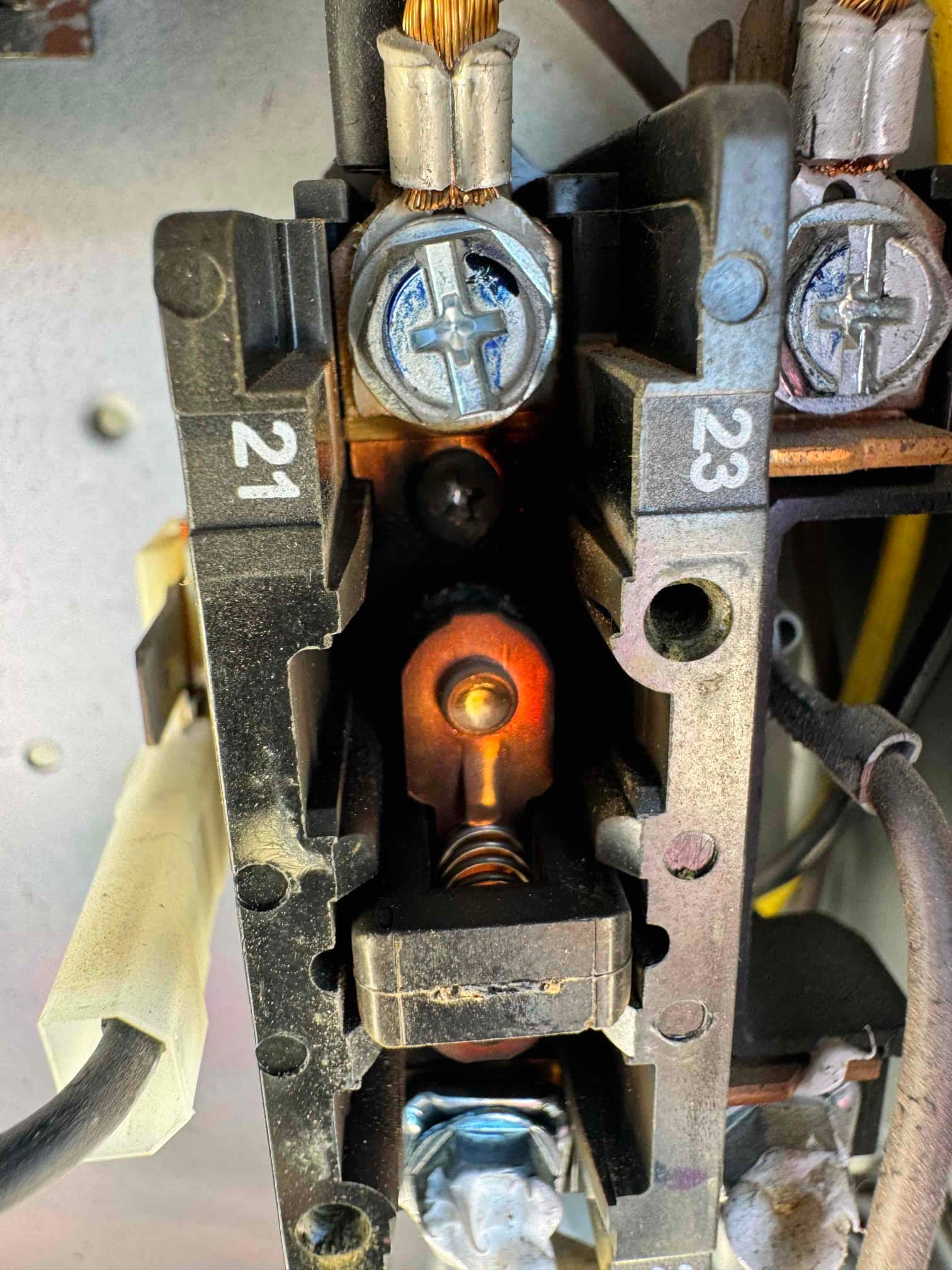 Contactor close-up showing copper contact and spring, with wires secured under screw lugs labeled 21 and 23.