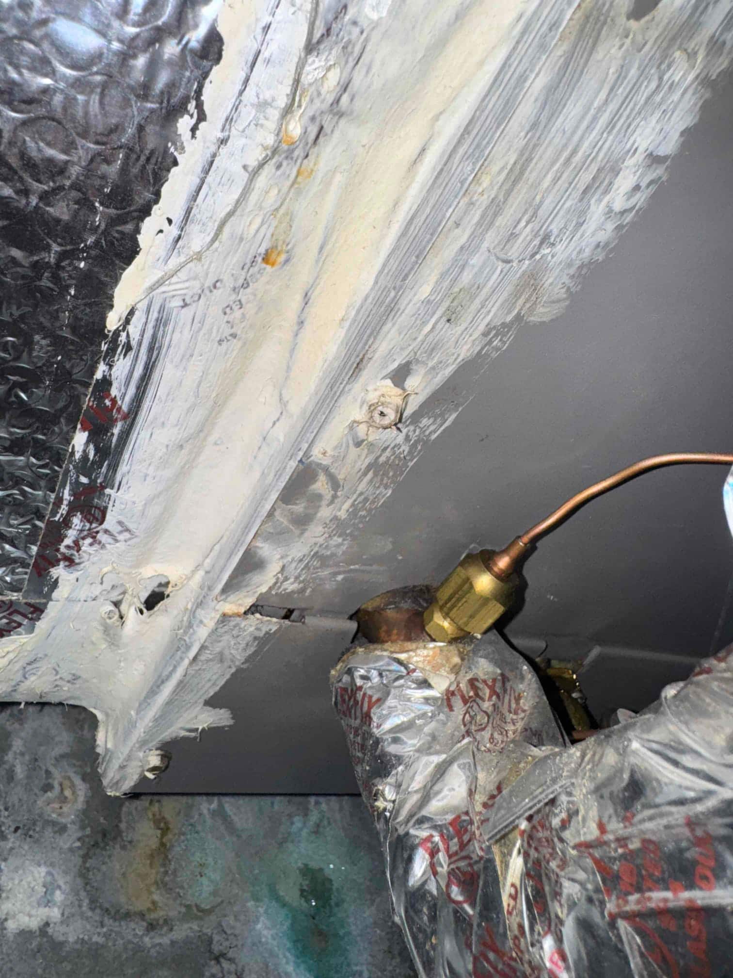 Copper refrigerant line with brass fitting enters the air handler cabinet, with mastic-sealed seams and wrapped suction line insulation.