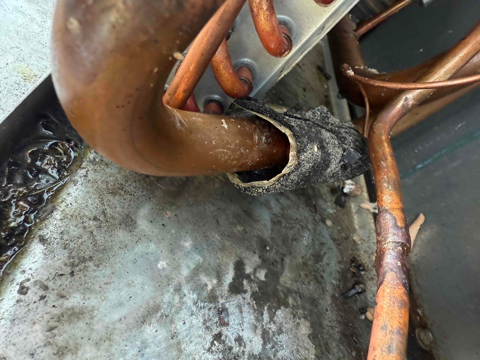 Copper refrigerant lines at evaporator coil with worn foam insulation and visible brazed joints sitting above a wet drain pan.