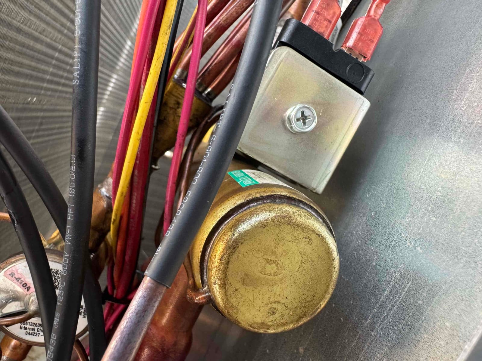 Copper refrigerant lines with red, yellow, and black wiring, and a small electrical module mounted on the interior panel.