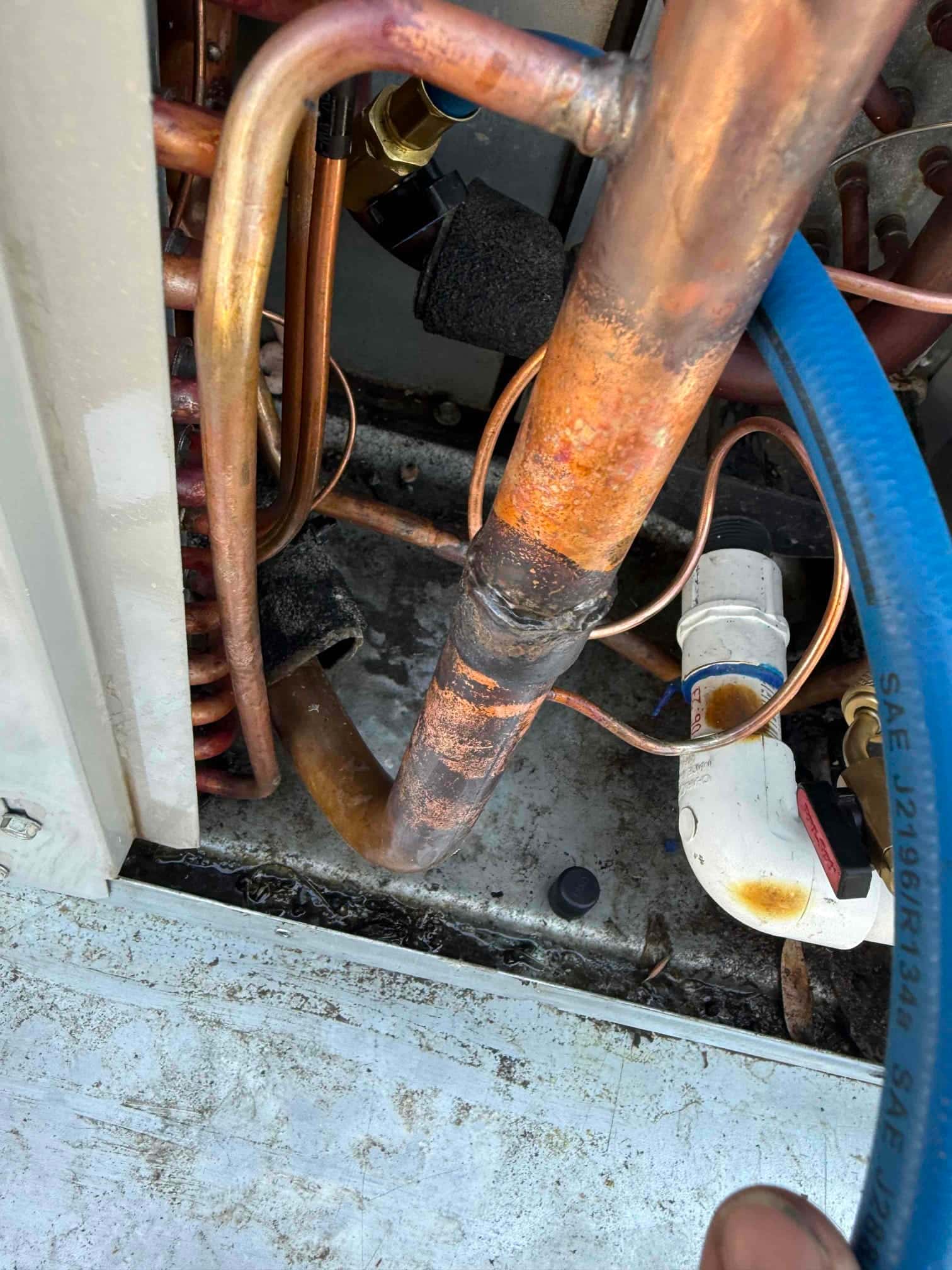 Copper refrigerant lines and service ports inside the outdoor unit, with a blue service hose attached and insulation pieces.