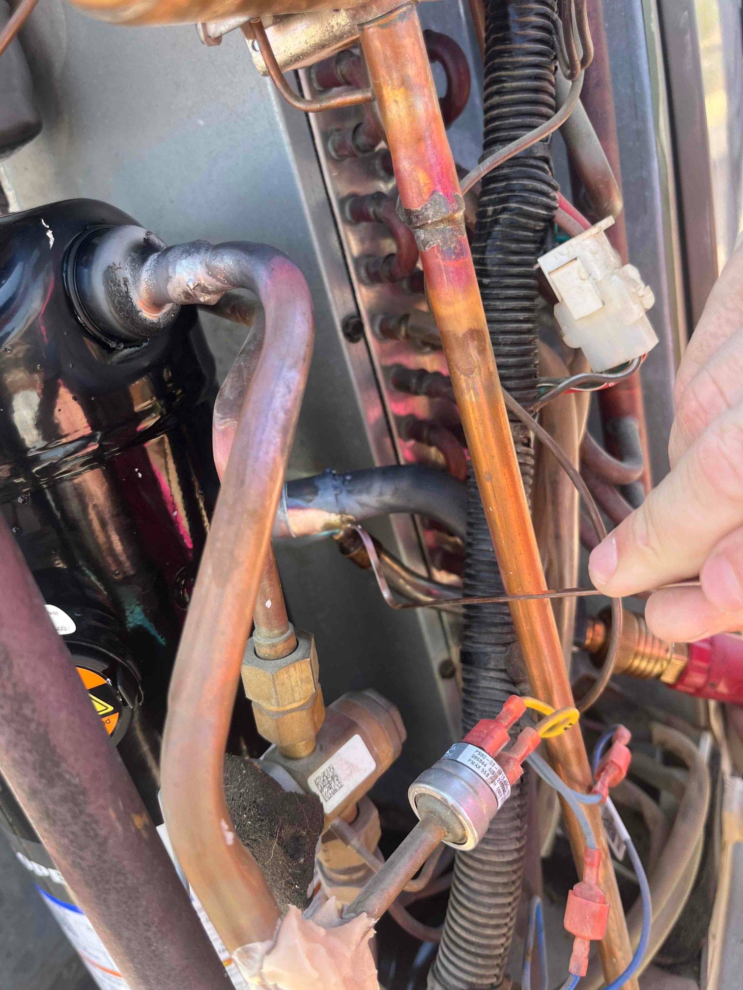 Copper refrigerant lines, service valve, and pressure switch wiring inside an outdoor condenser, with technician hand holding a small wire.