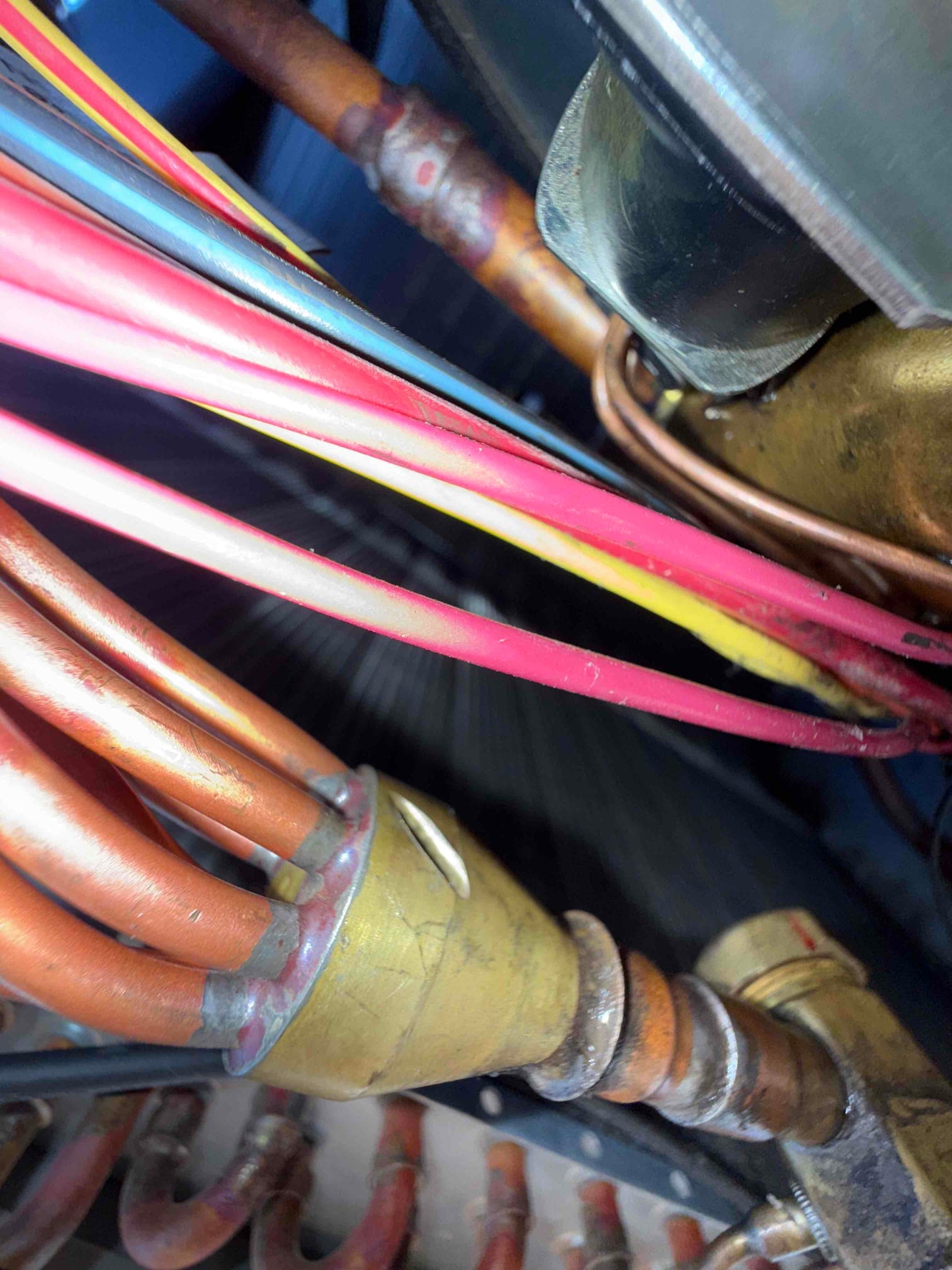 Copper refrigerant tubing and brass fitting with red, yellow, and blue control wires inside the unit.