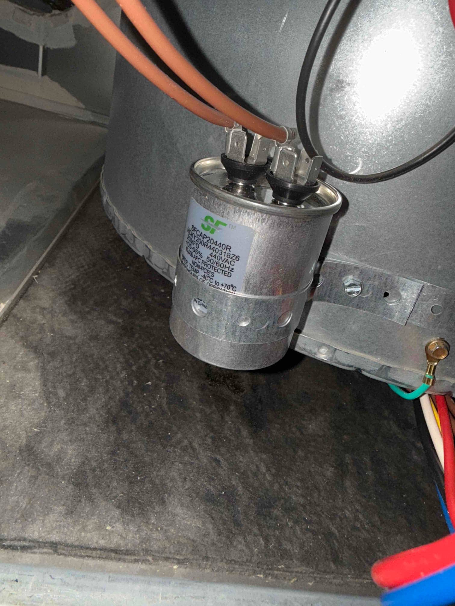 Cylindrical run capacitor mounted inside the unit, with two terminals connected and nearby wiring routed neatly.