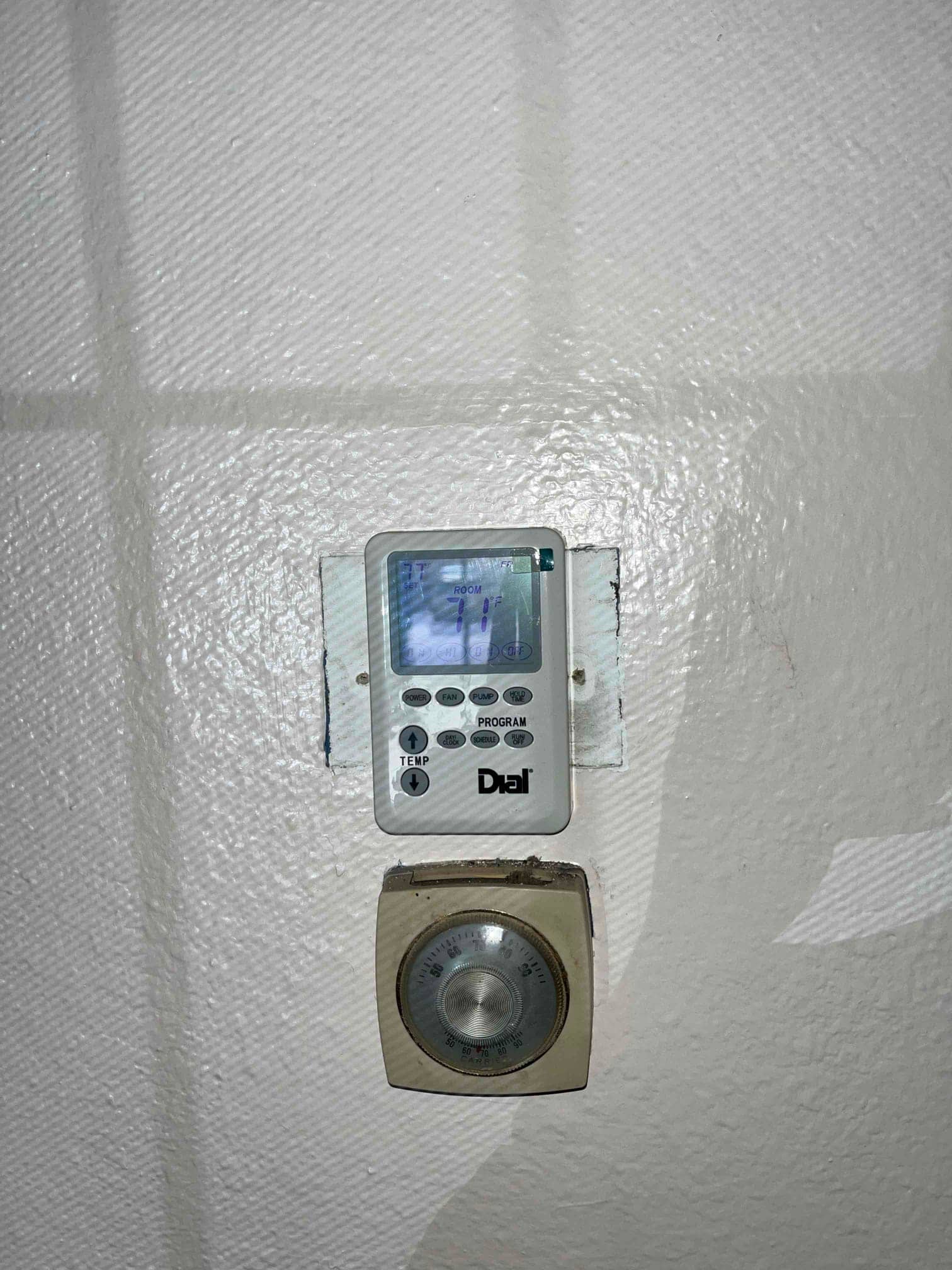Digital wall thermostat displays room temperature 71°F, mounted above an older mechanical dial thermostat on painted wall.