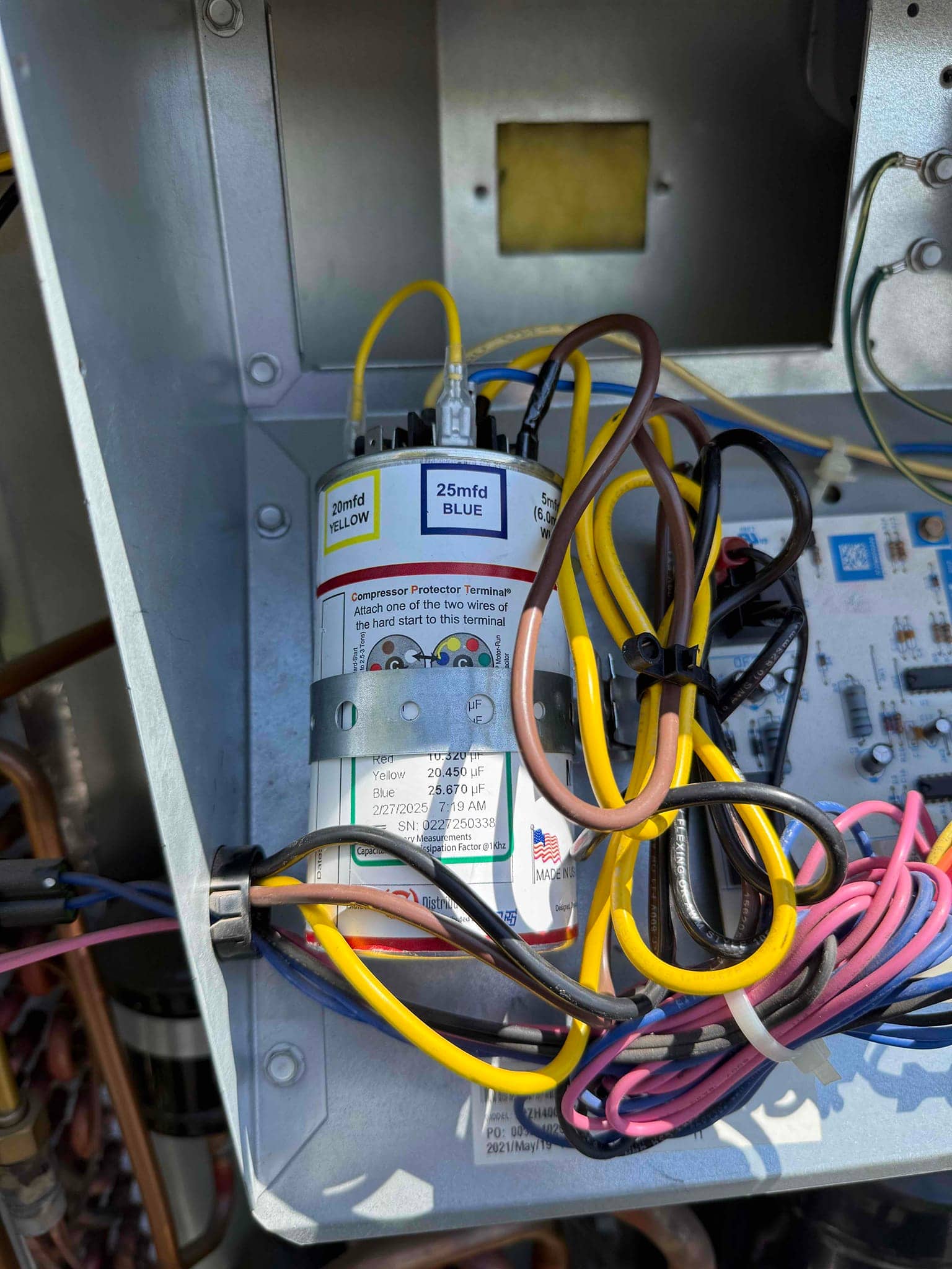 Dual-run capacitor labeled 20 mfd yellow and 25 mfd blue with multiple wires connected inside condenser control compartment.