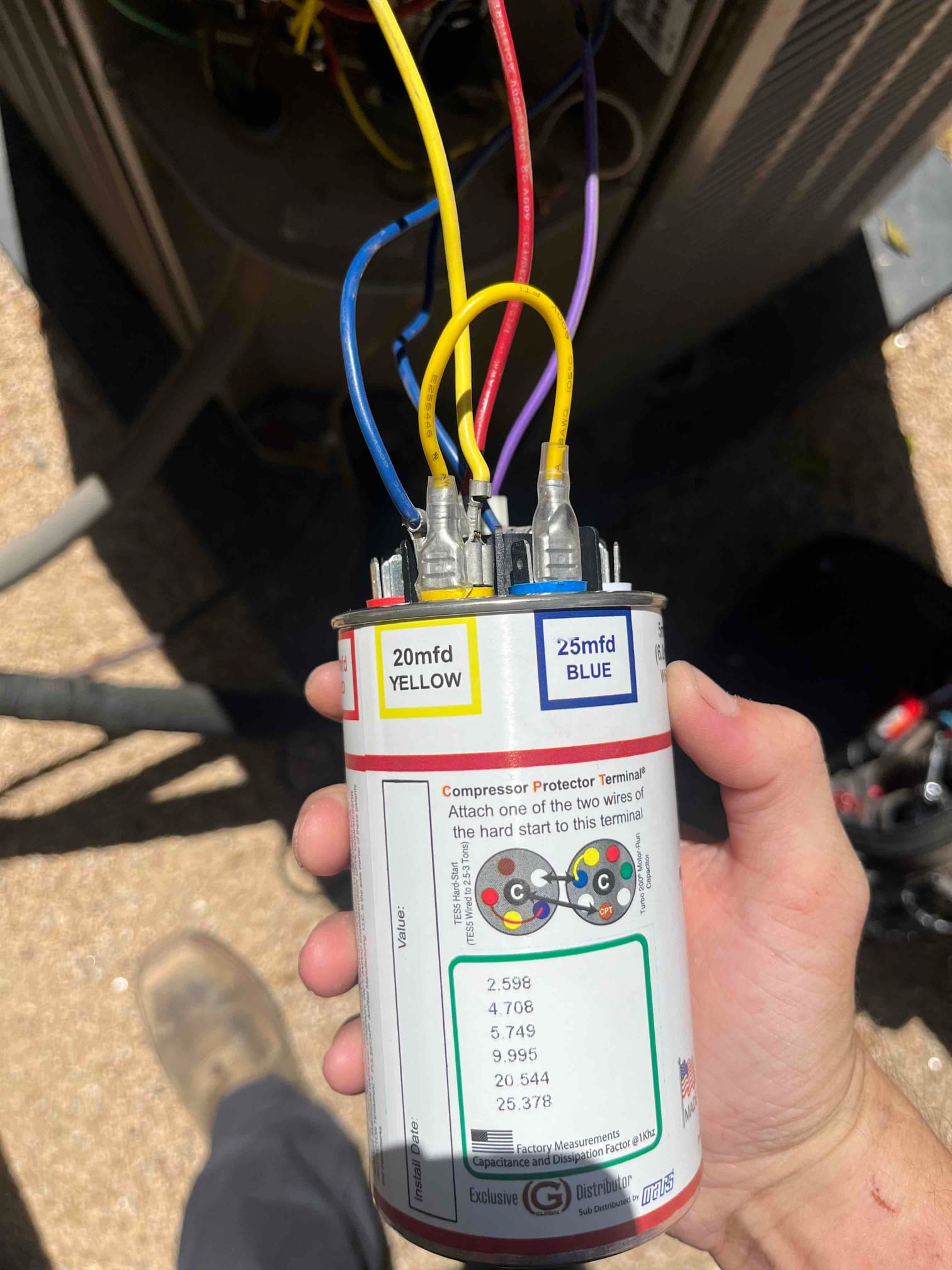 Dual-run capacitor labeled 20 mfd yellow and 25 mfd blue with wires connected to its terminals.