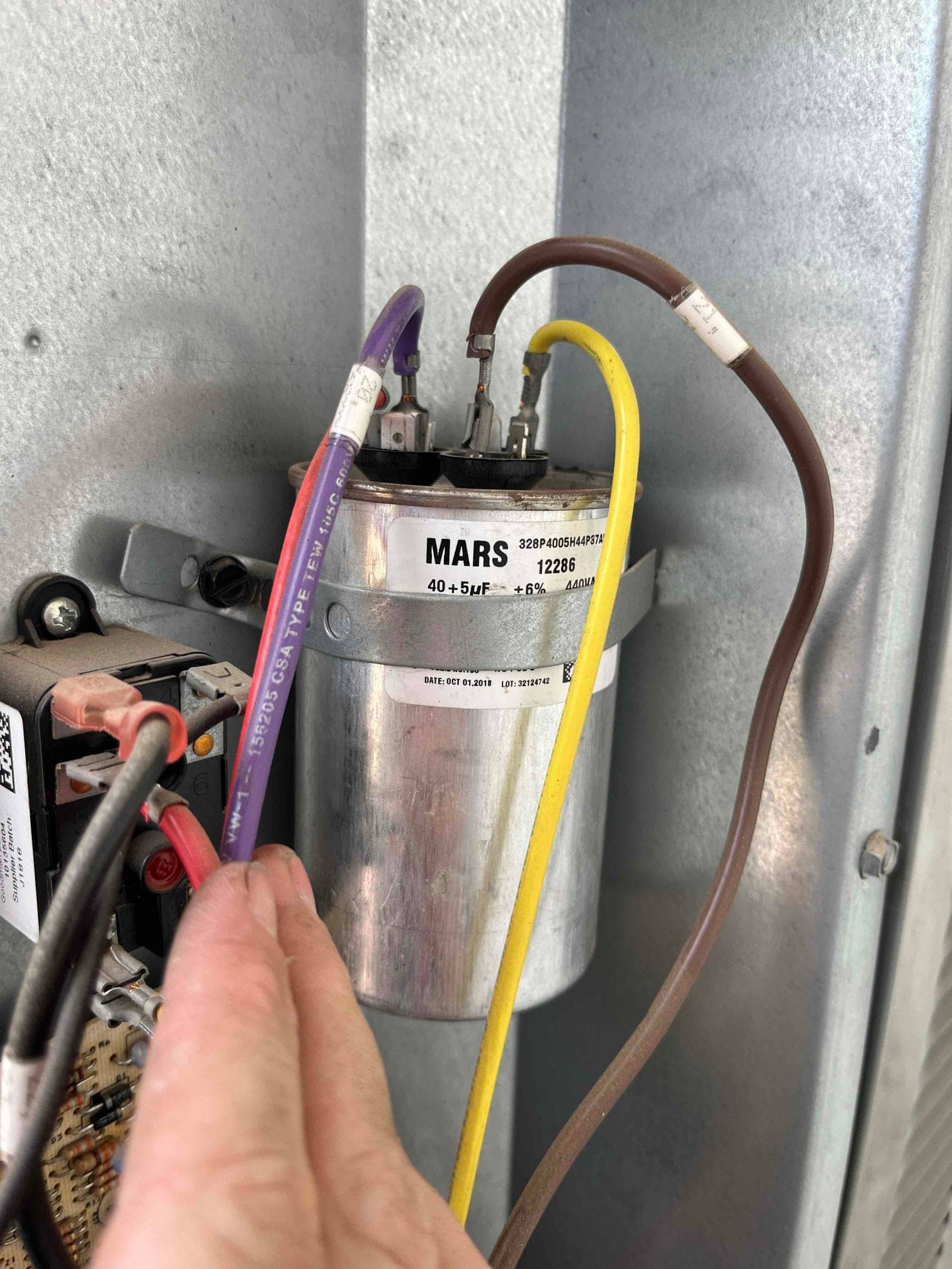 Dual-run capacitor labeled 40/5 μF ±6% 440VAC with brown, yellow, and purple wires connected to its terminals inside the cabinet.