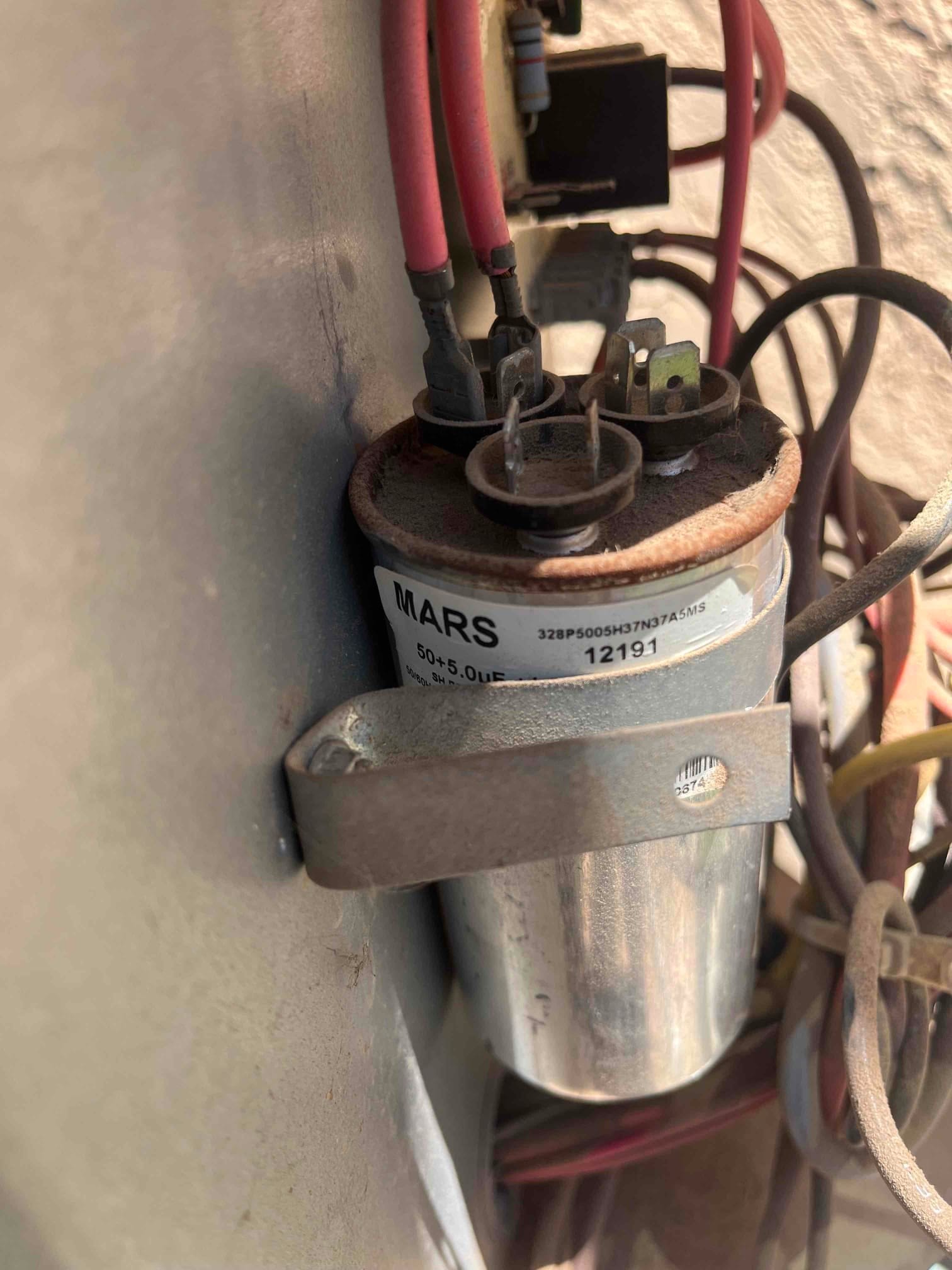 Dual-run capacitor labeled 50+5.0 μF mounted with wires on its terminals and visible rust at top.