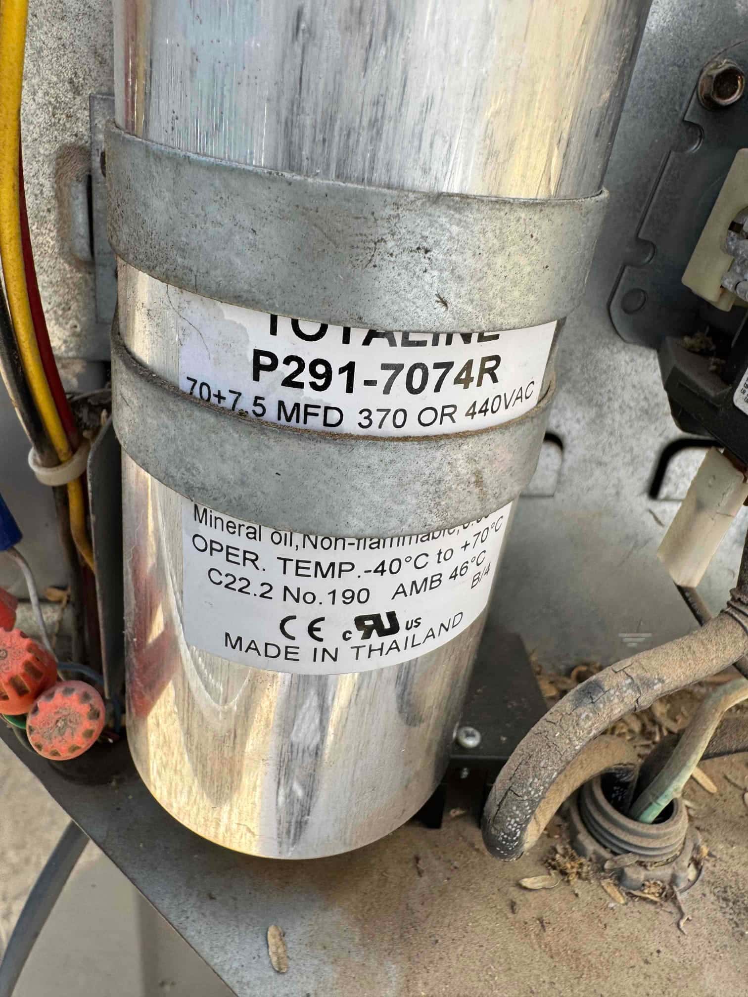Dual-run capacitor labeled 70+7.5 MFD 370 or 440 VAC secured with metal strap and wiring.