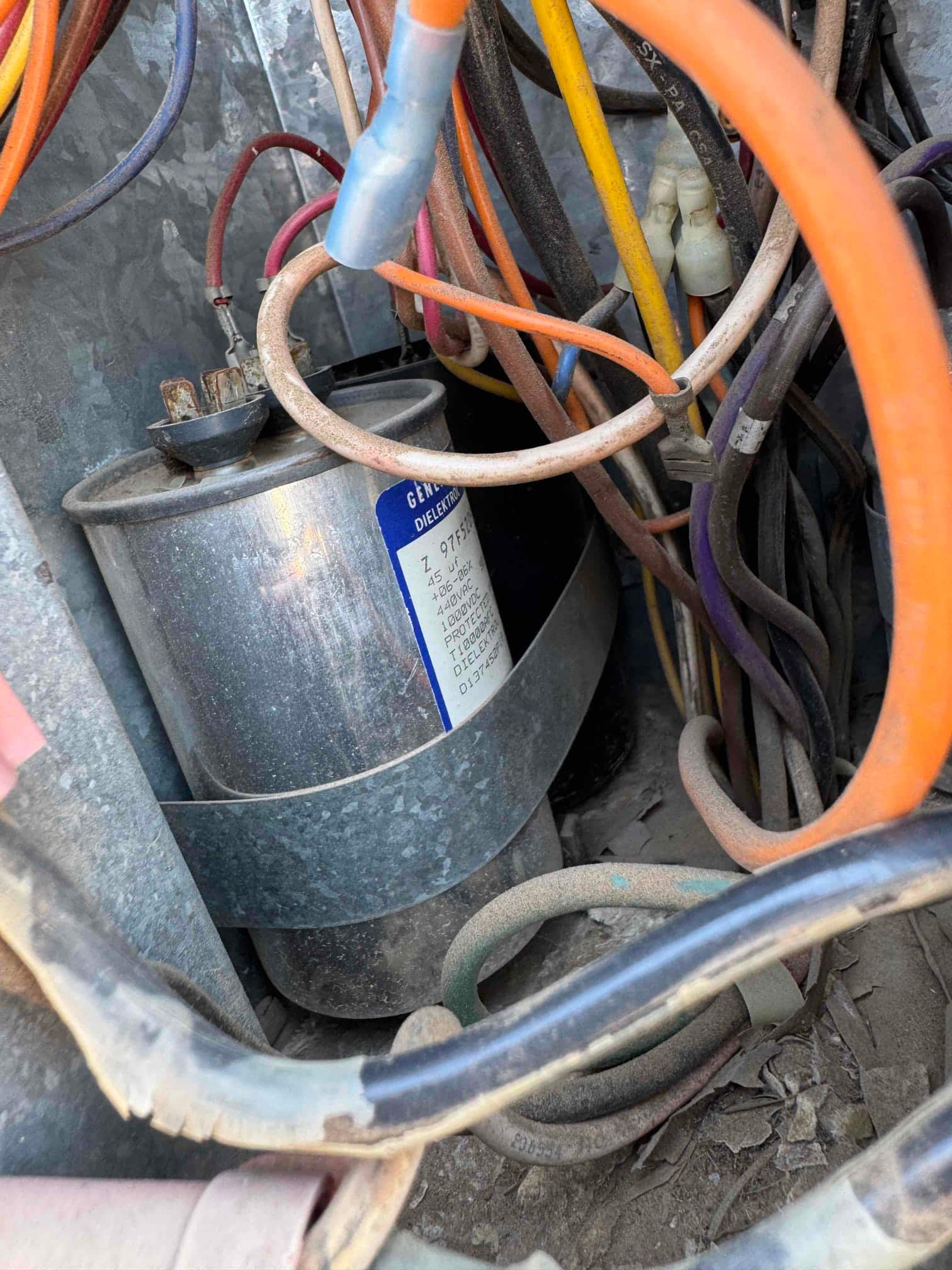 Dusty dual-run capacitor labeled 45/5 μF 440 VAC with wires connected to its terminals inside the outdoor unit.