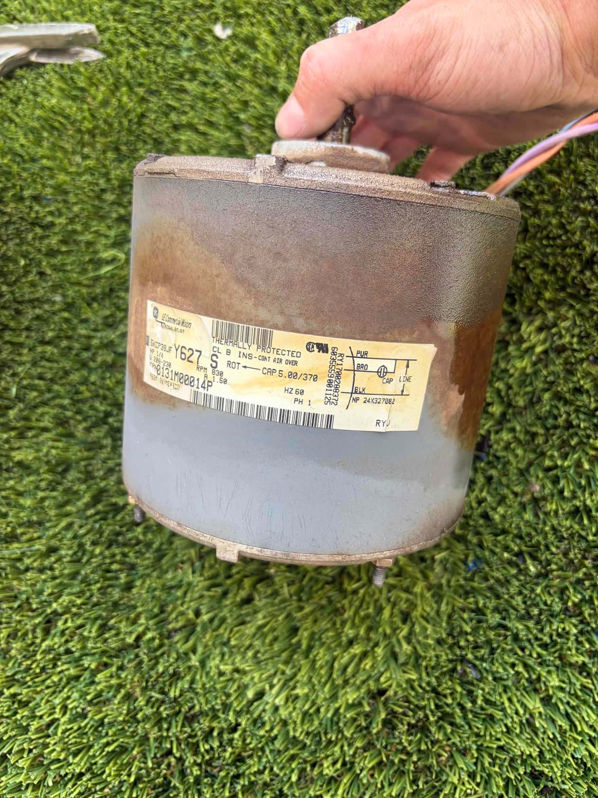 Electric motor removed from HVAC equipment, showing rust and discoloration on the housing with wiring and a printed specification label.