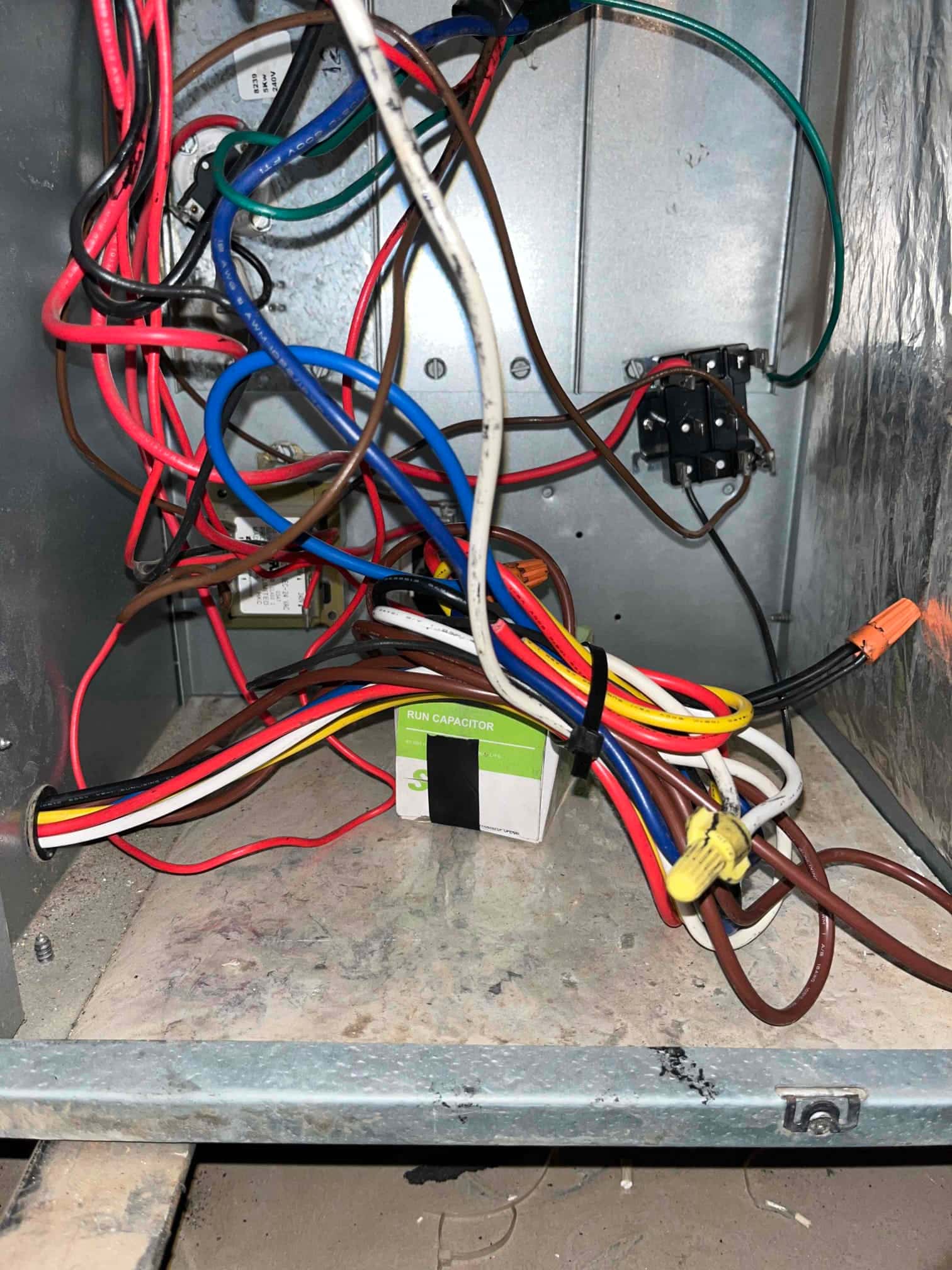 Electrical compartment of indoor unit with multiple colored wires, wire nuts, and a boxed run capacitor.