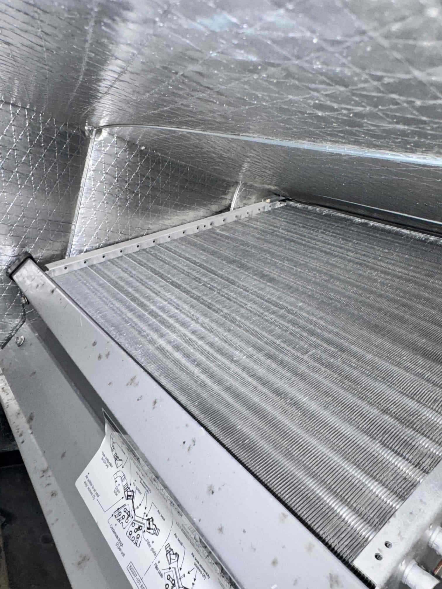 Evaporator coil in an air handler cabinet, showing aluminum fins and foil-faced insulated duct liner.