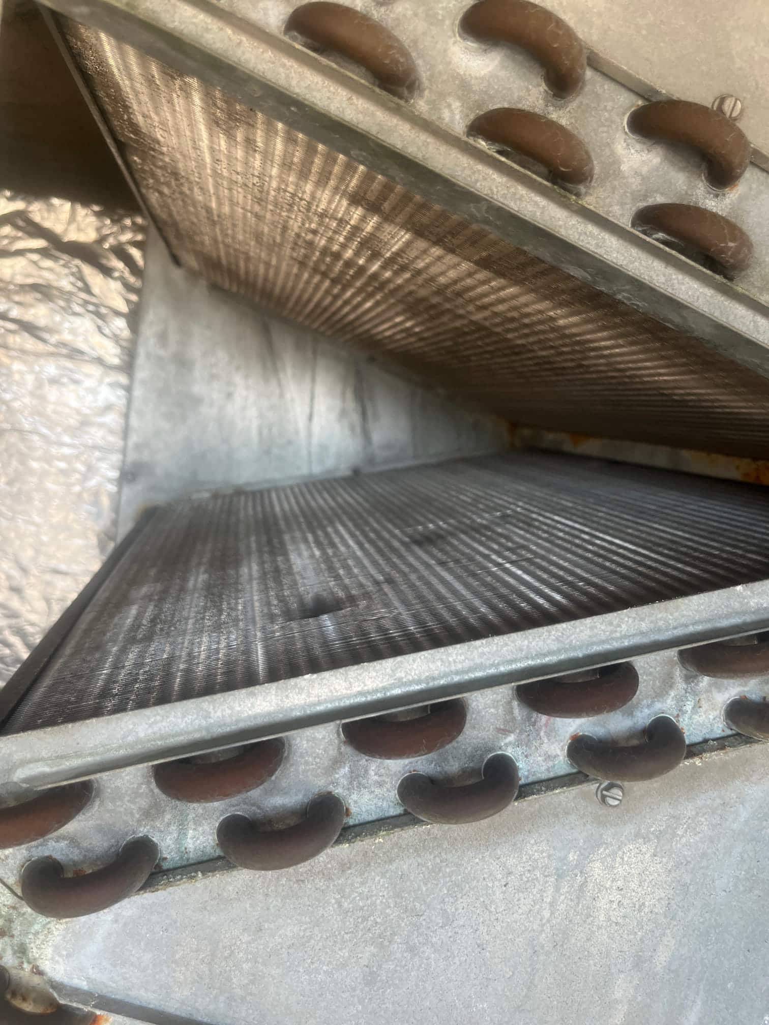 Evaporator A-coil assembly with copper U-bends and aluminum fins inside the air handler cabinet, surfaces appear clean.