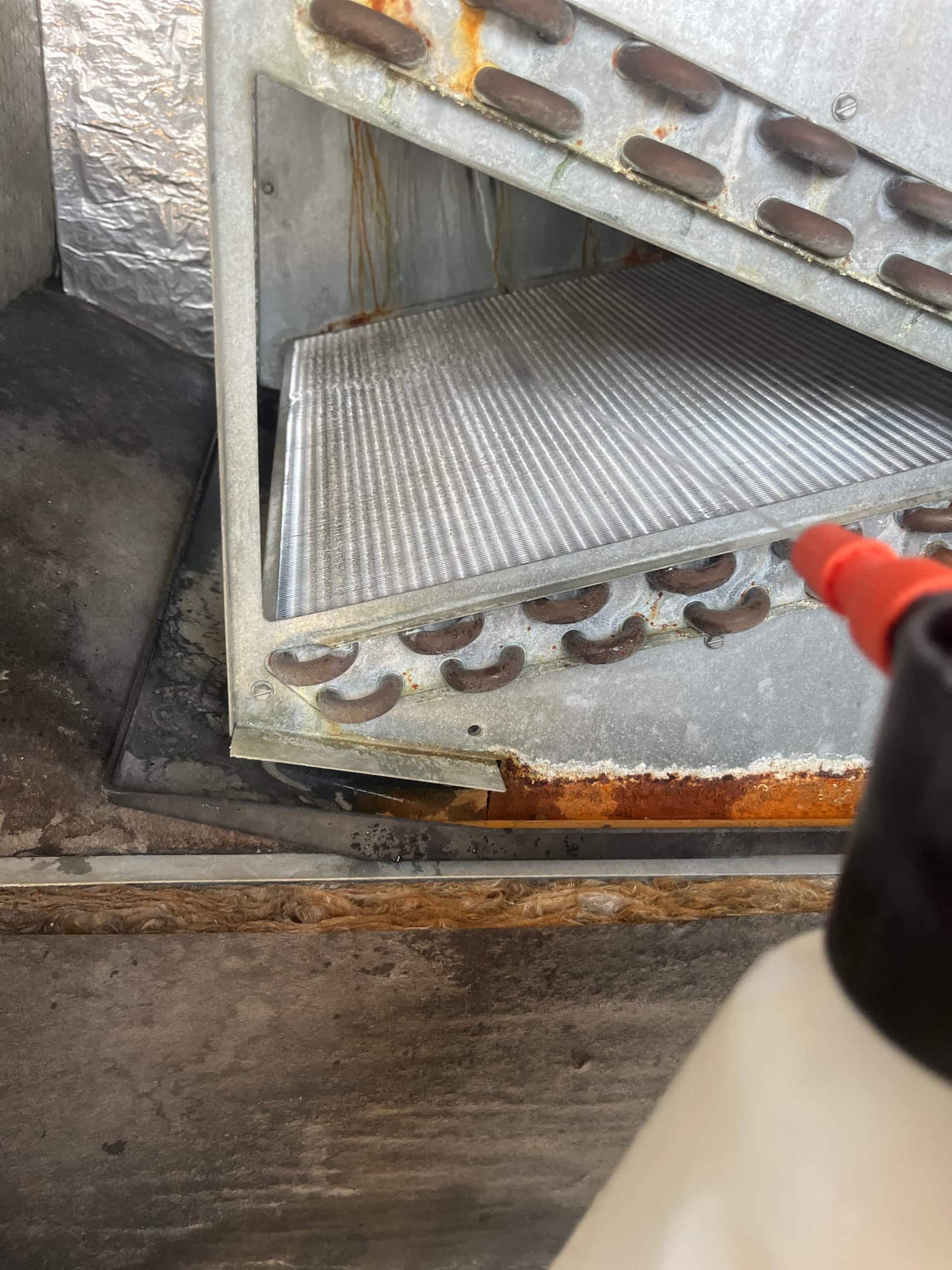 Evaporator coil assembly with fin pack exposed, showing rust along the drain pan edge and copper tube connections.