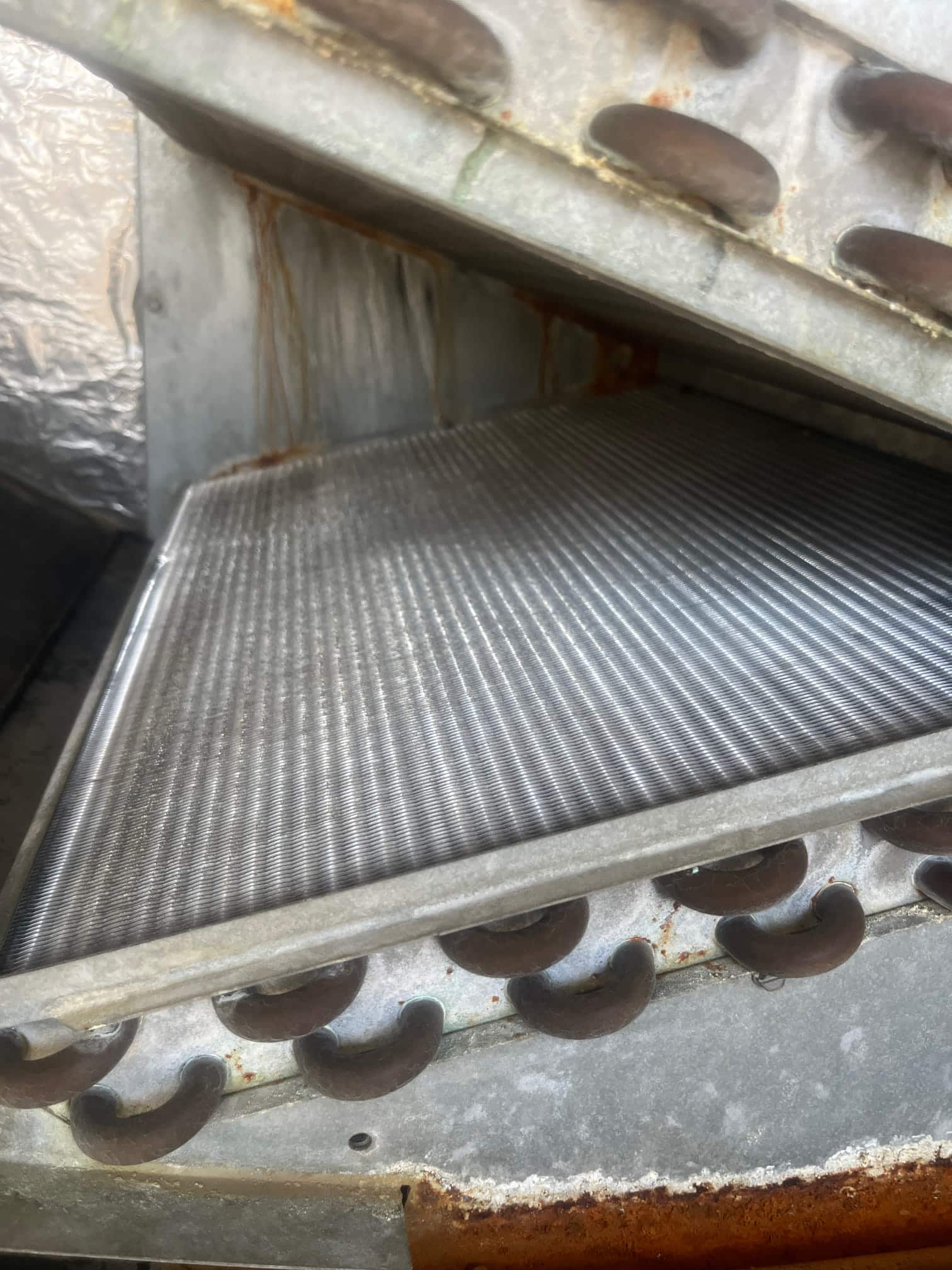 Evaporator coil assembly inside the air handler, showing finned surface, copper U-bends, and light rust on the housing.