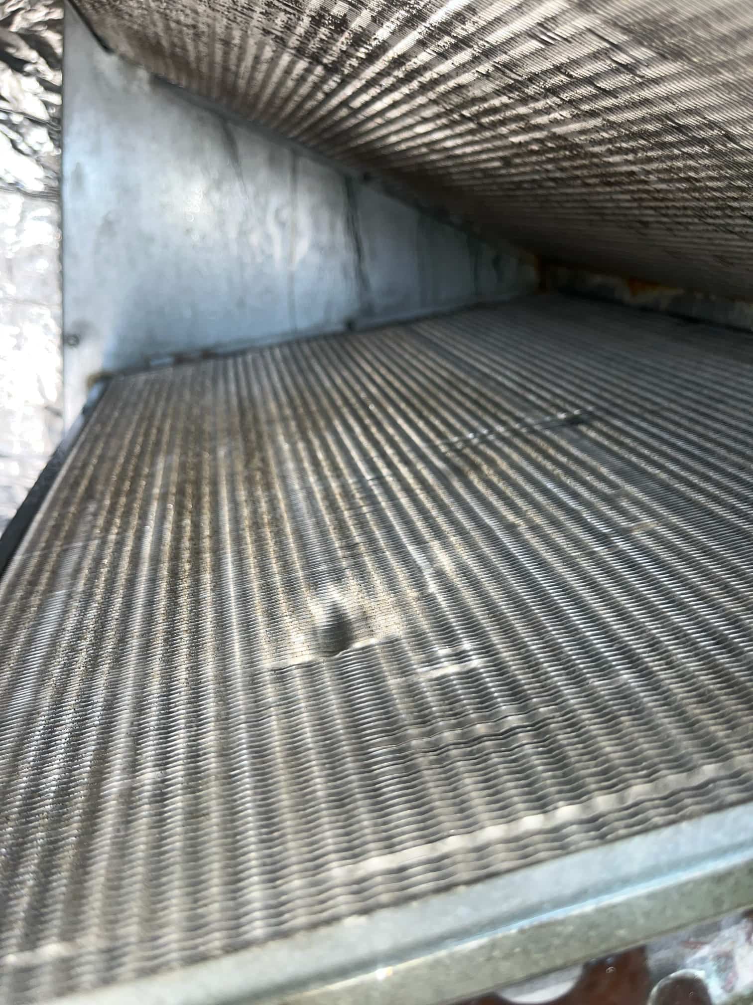 Evaporator coil fins inside the air handler, showing uniform fin pattern with small dents.