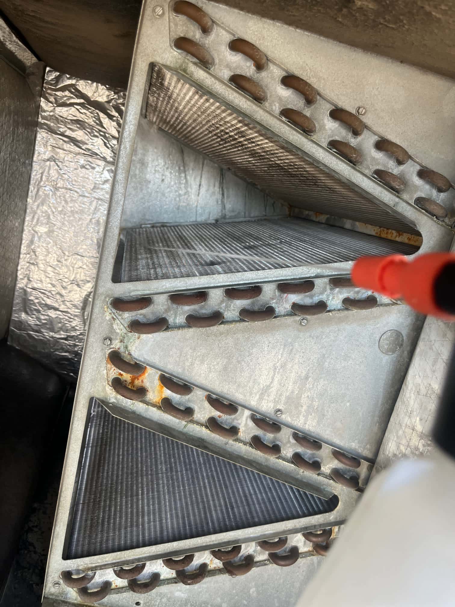Evaporator A-coil inside air handler with copper tubing and fins, showing surface rust on headers.