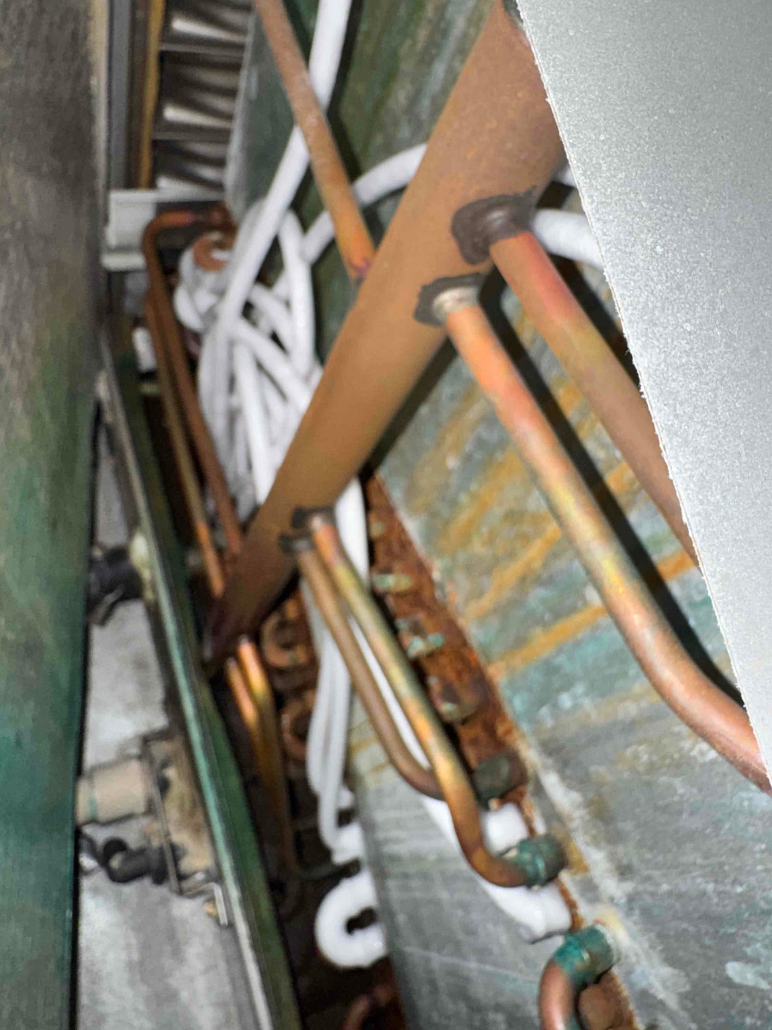 Evaporator coil section with copper refrigerant tubing, white insulated lines, and visible rust and oxidation.