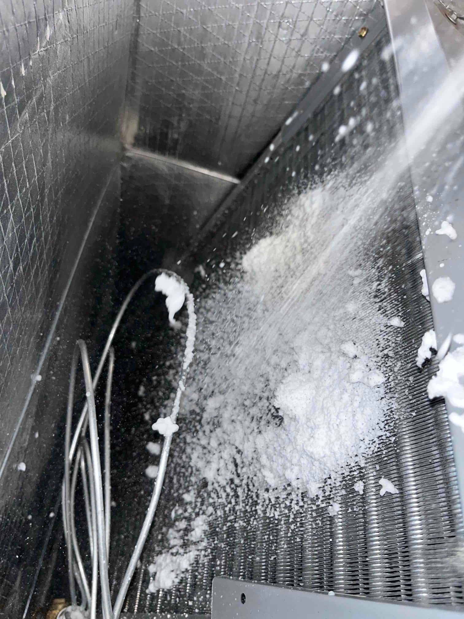Evaporator coil surface shows significant ice accumulation and frost inside the metal air handler cabinet.