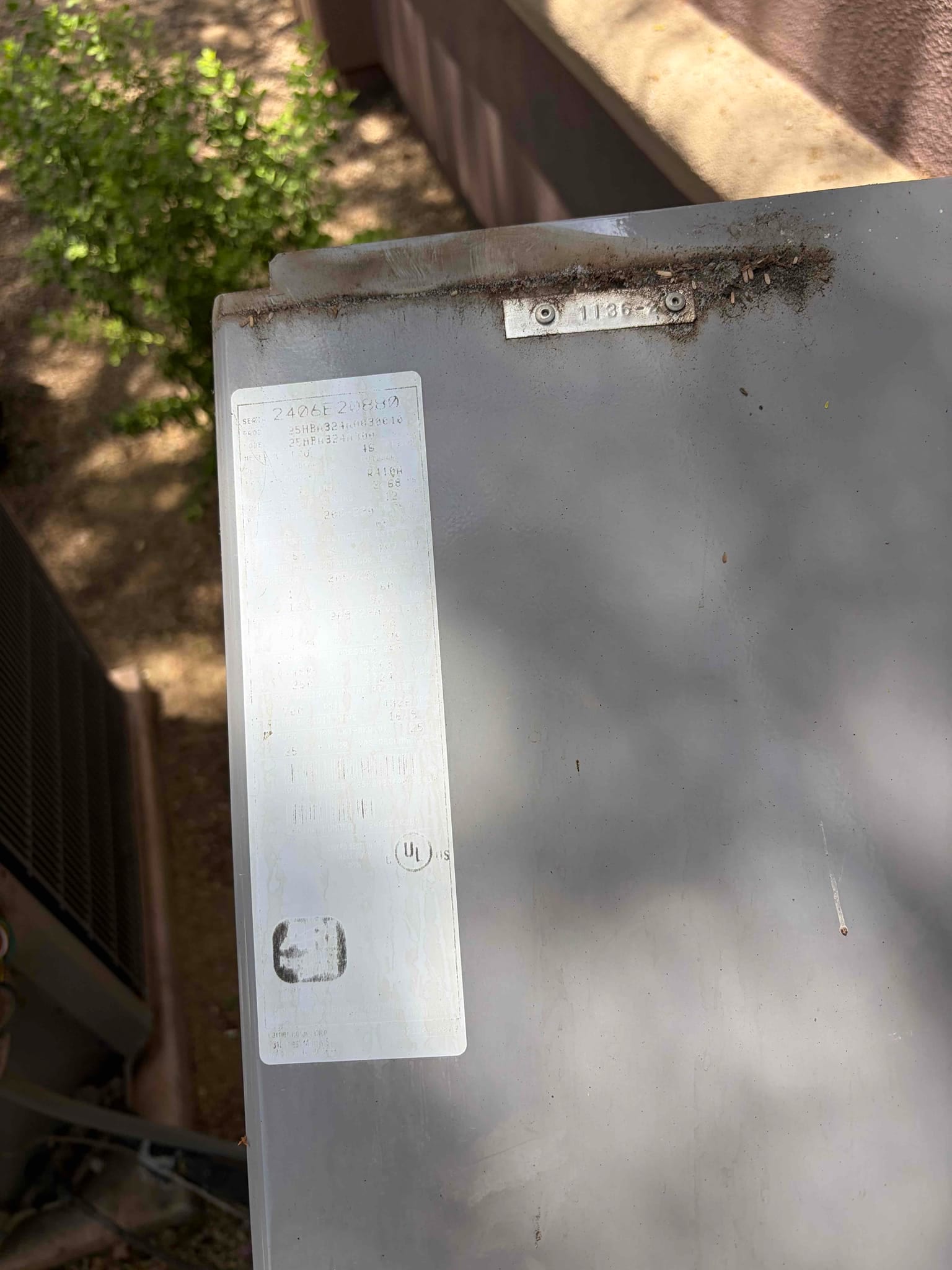 Faded equipment label on the top panel of an outdoor condenser cabinet near the wall.