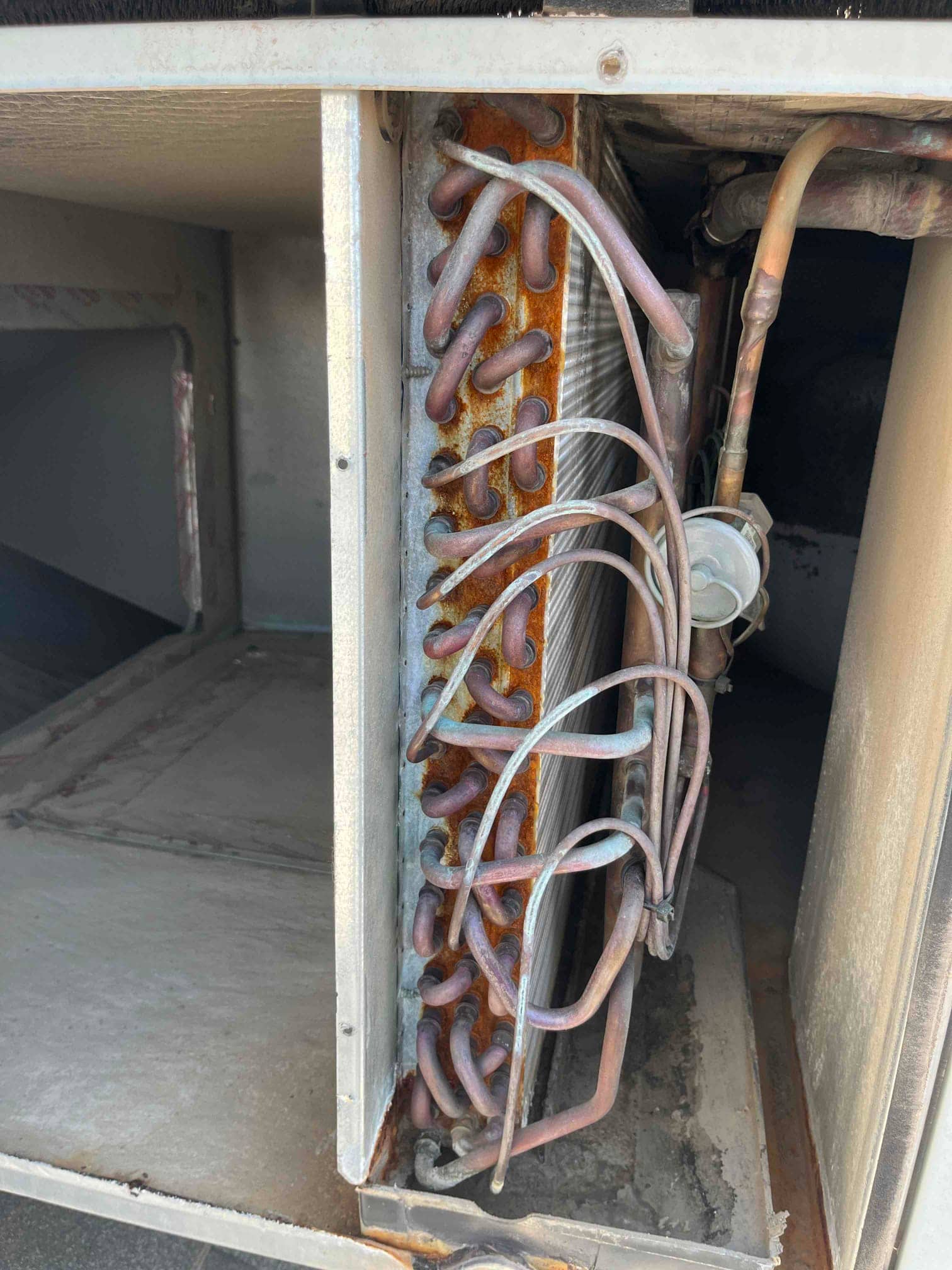 Fin-and-tube coil with copper refrigerant tubing and visible rust on the steel support plate.